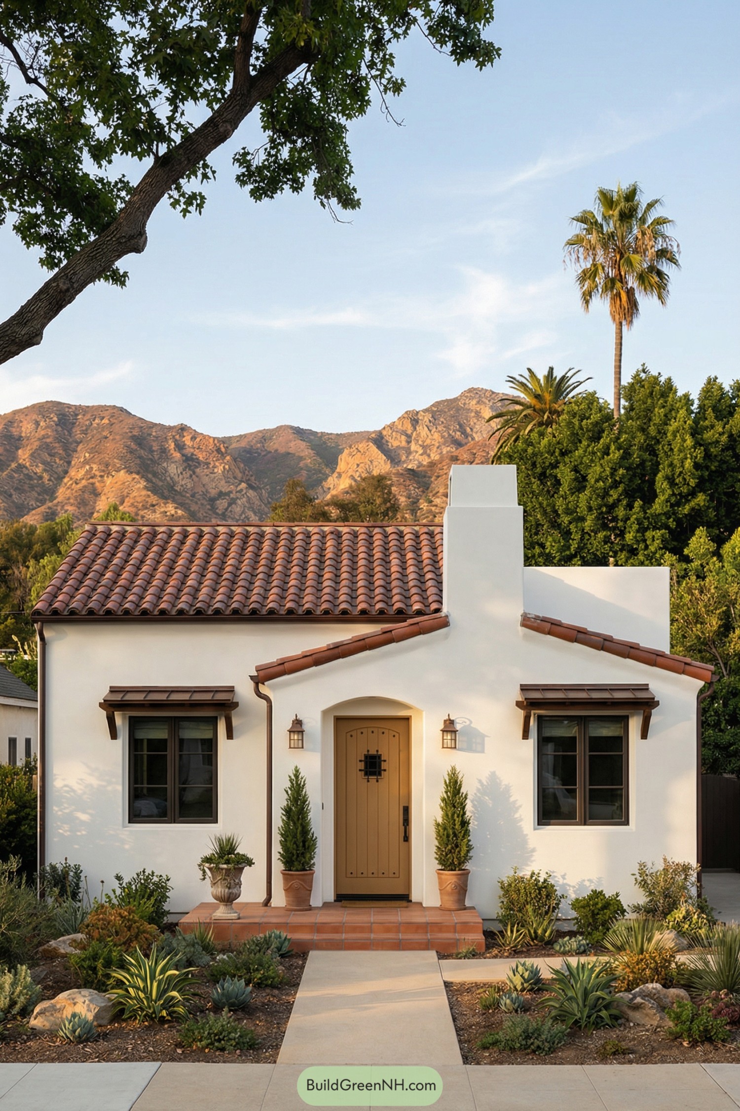 Small white stucco Spanish cottage with red tile roof, arched entry, and drought tolerant front garden against mountain backdrop
