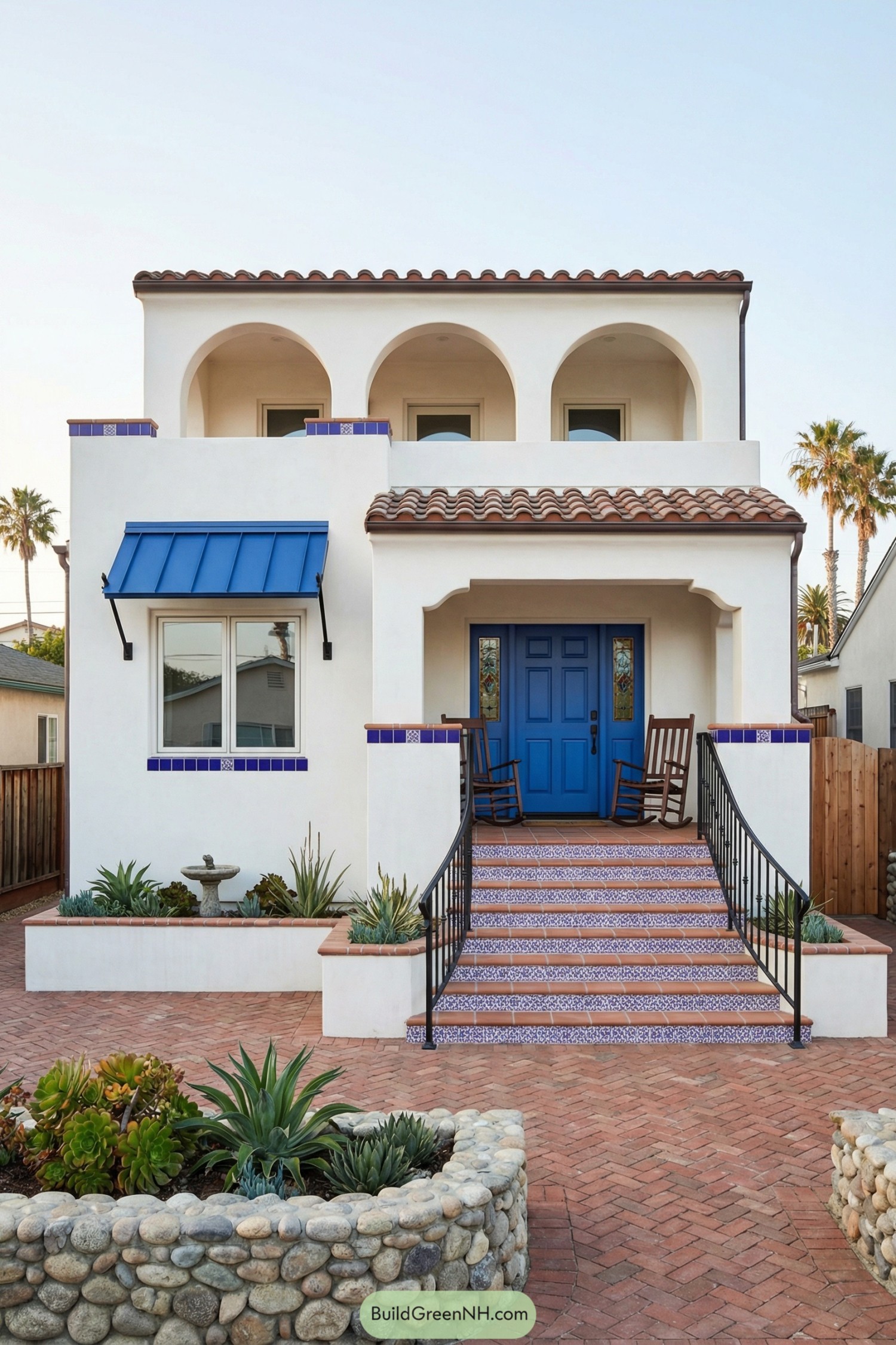 White stucco Spanish bungalow with bright blue door terracotta roof tiles and patterned tile steps