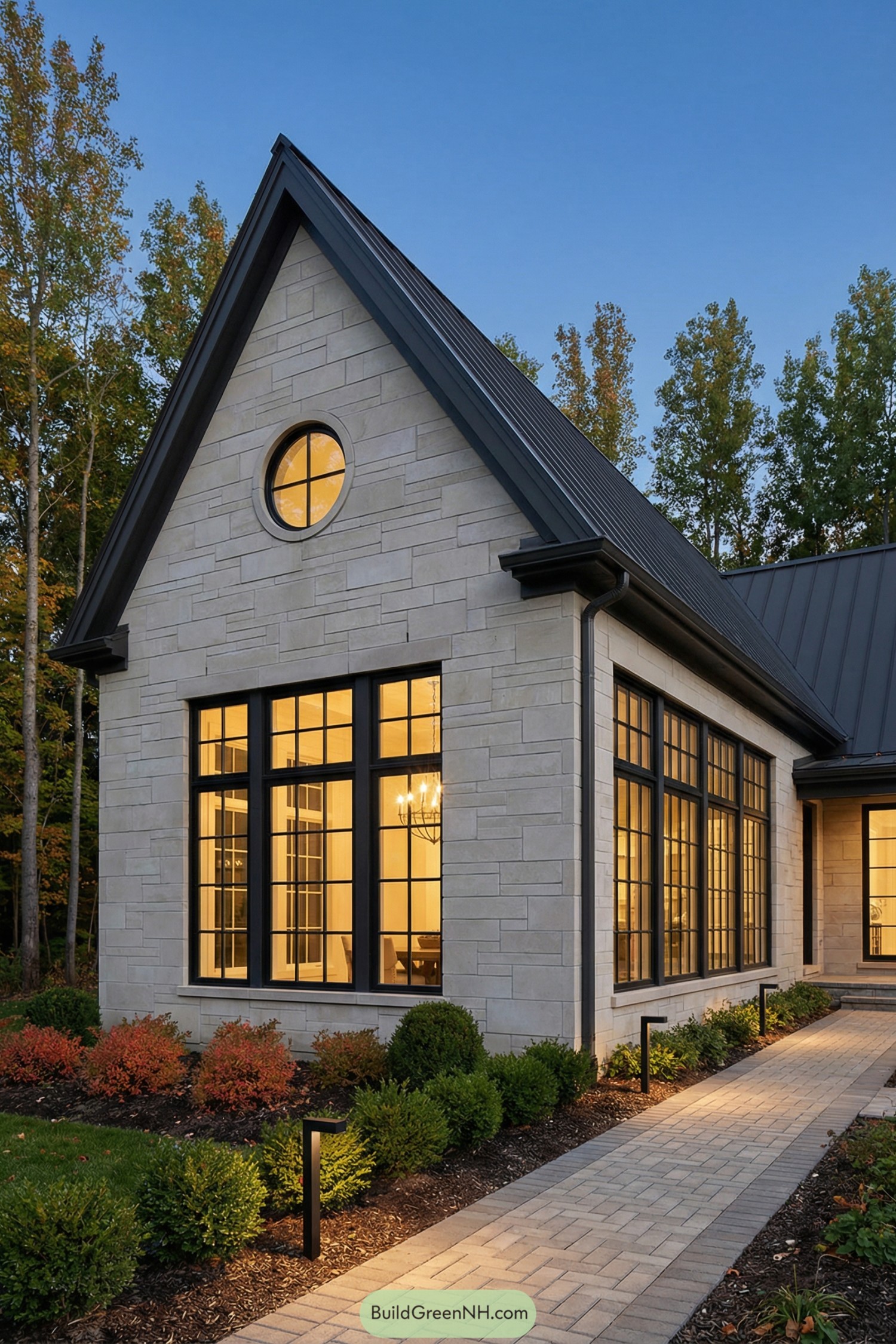 Stone clad gabled house with large black framed windows and a paved entry walk