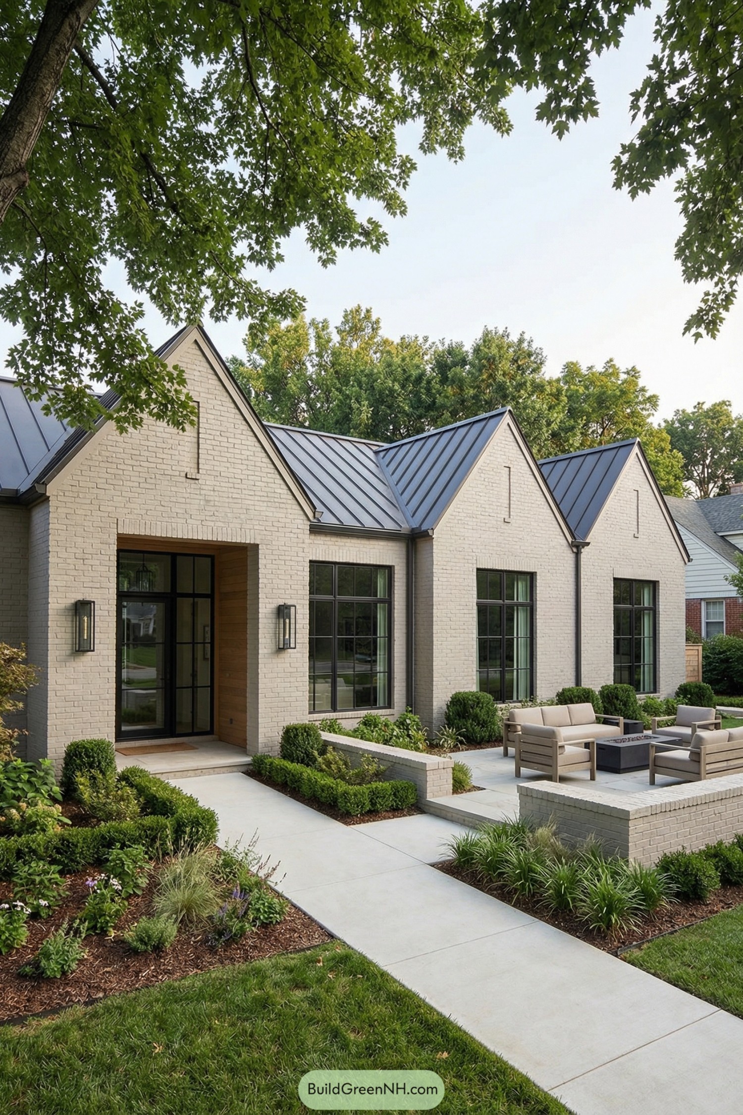 Single story brick house with tall gables, large black-framed windows, and a landscaped front patio with outdoor seating
