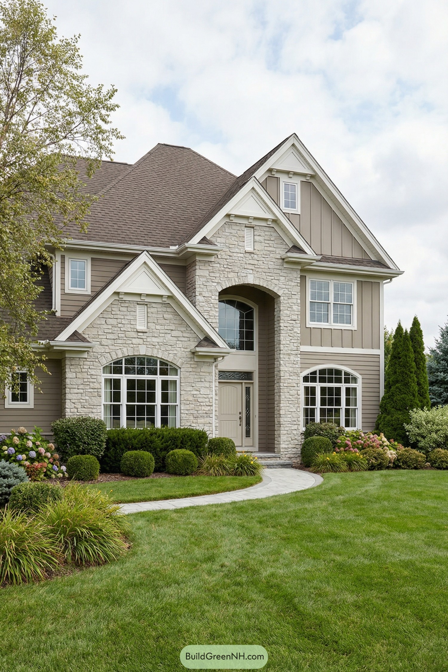 Two story taupe house with stone facade, arched entry, and manicured front lawn