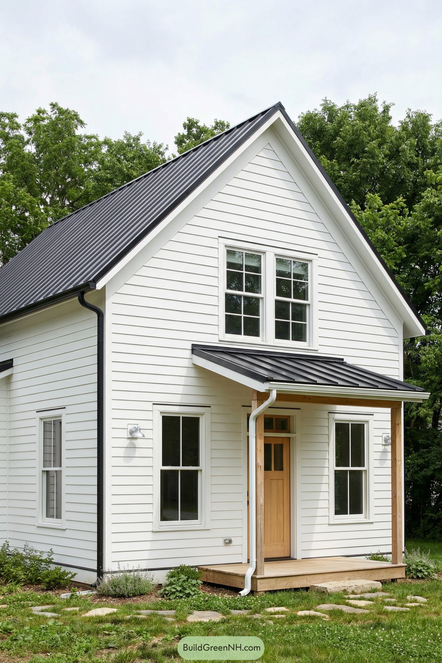 White clapboard cottage with black metal roof and small wood porch