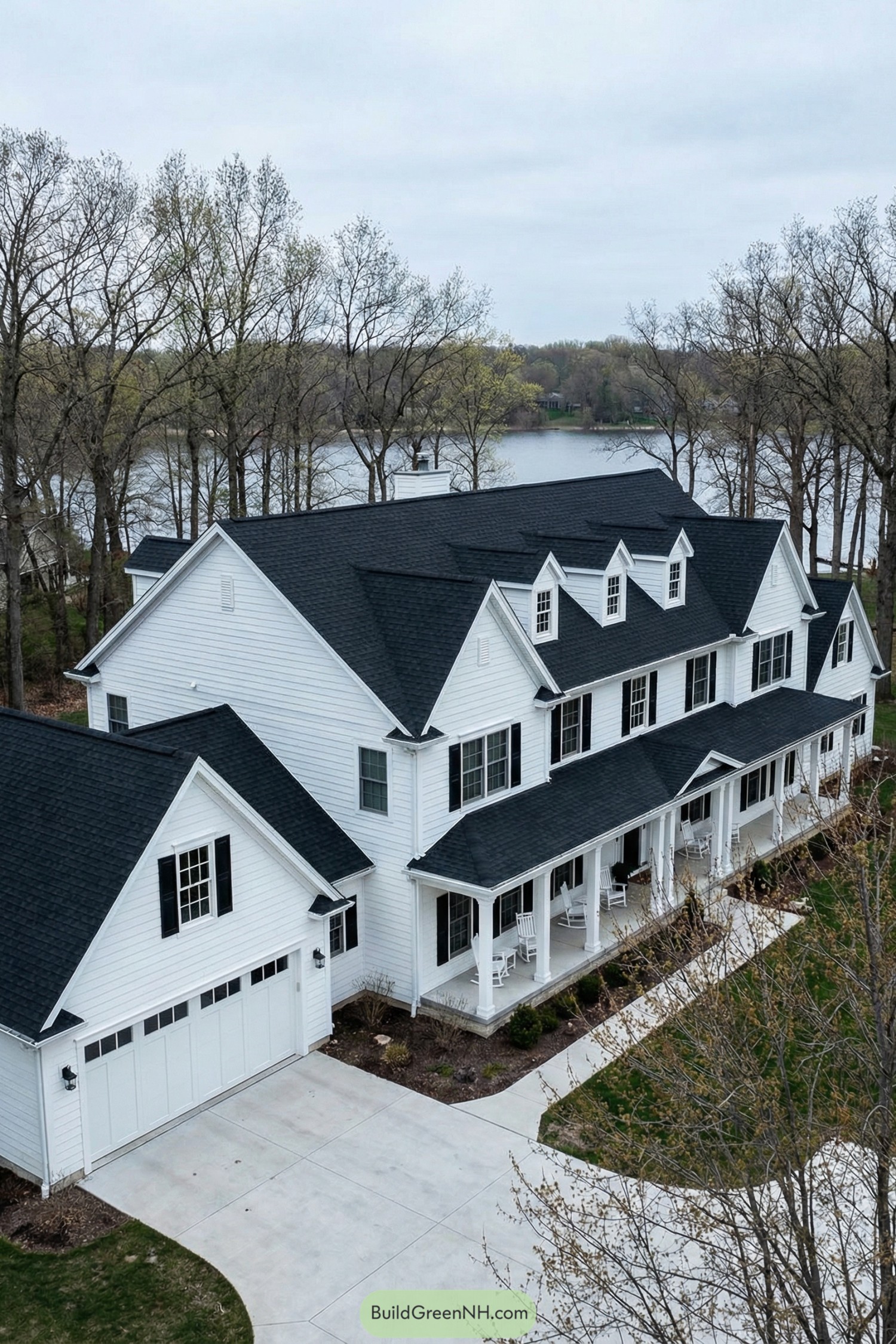 White colonial style house with black roof by a lake