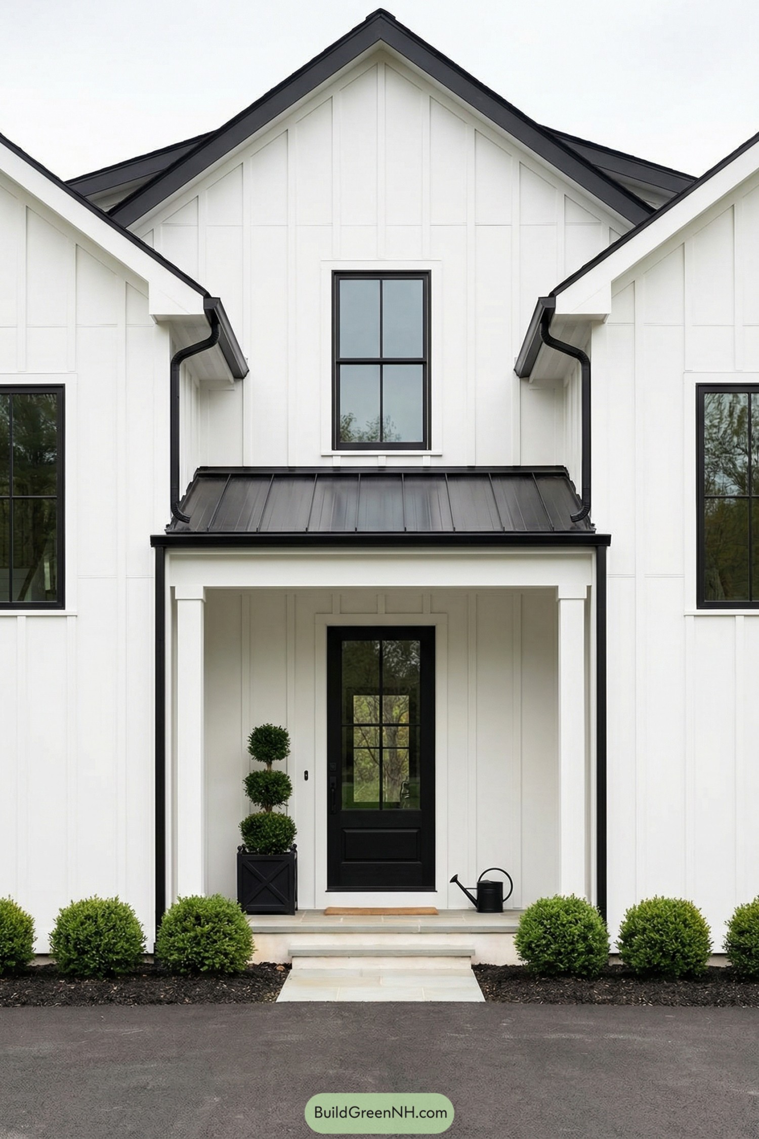 White modern farmhouse entry with black metal roof, black framed windows, and simple greenery