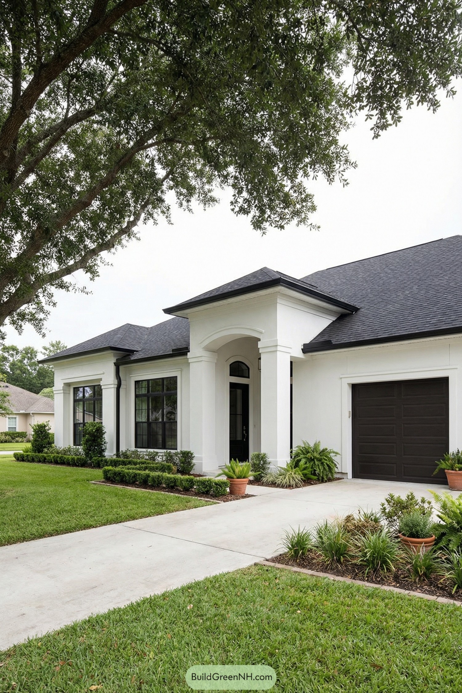White stucco house with black roof and large black framed windows, framed by neat lawn and potted plants