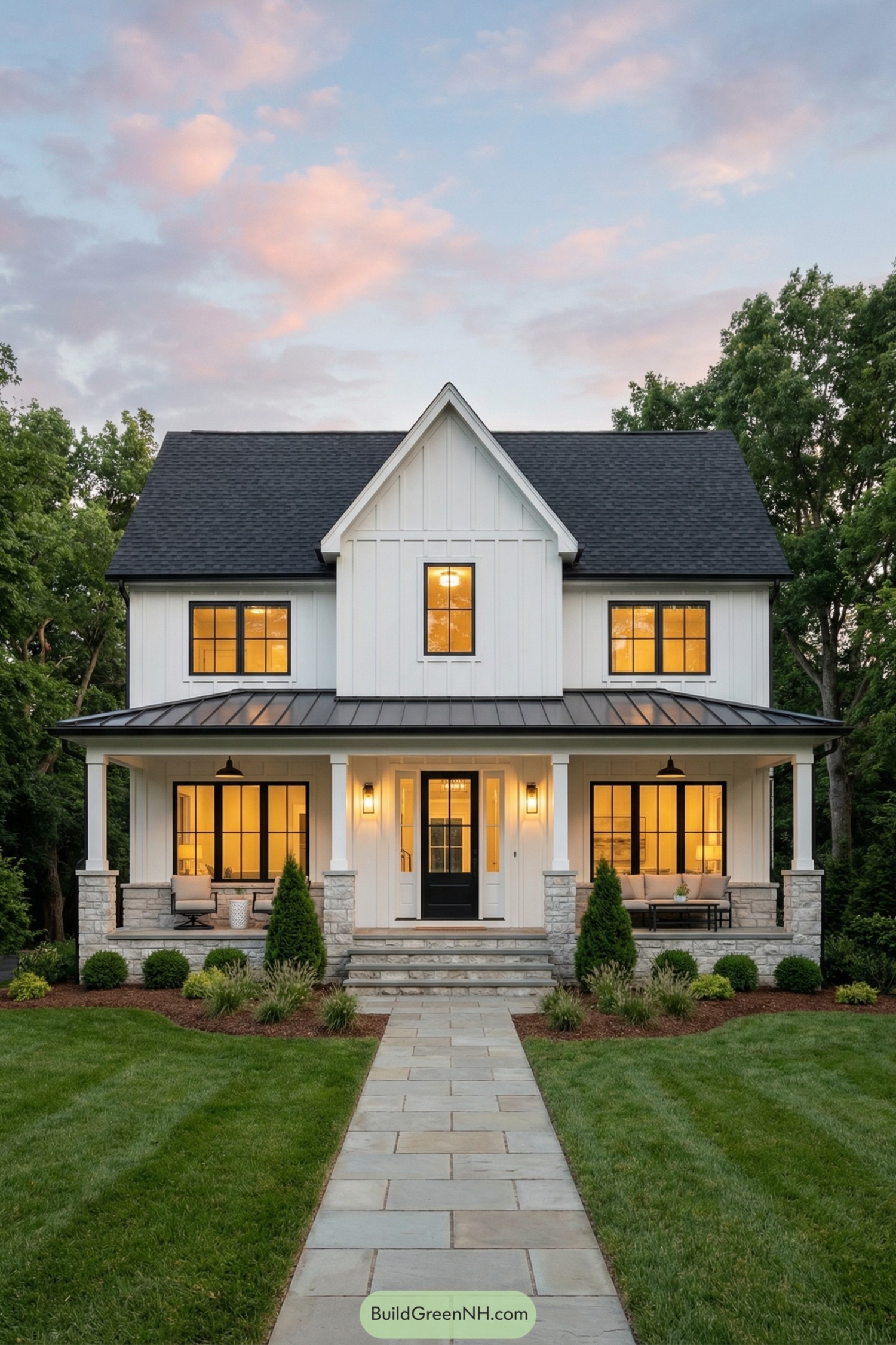 White two story farmhouse with black roof, front porch, and manicured lawn at dusk