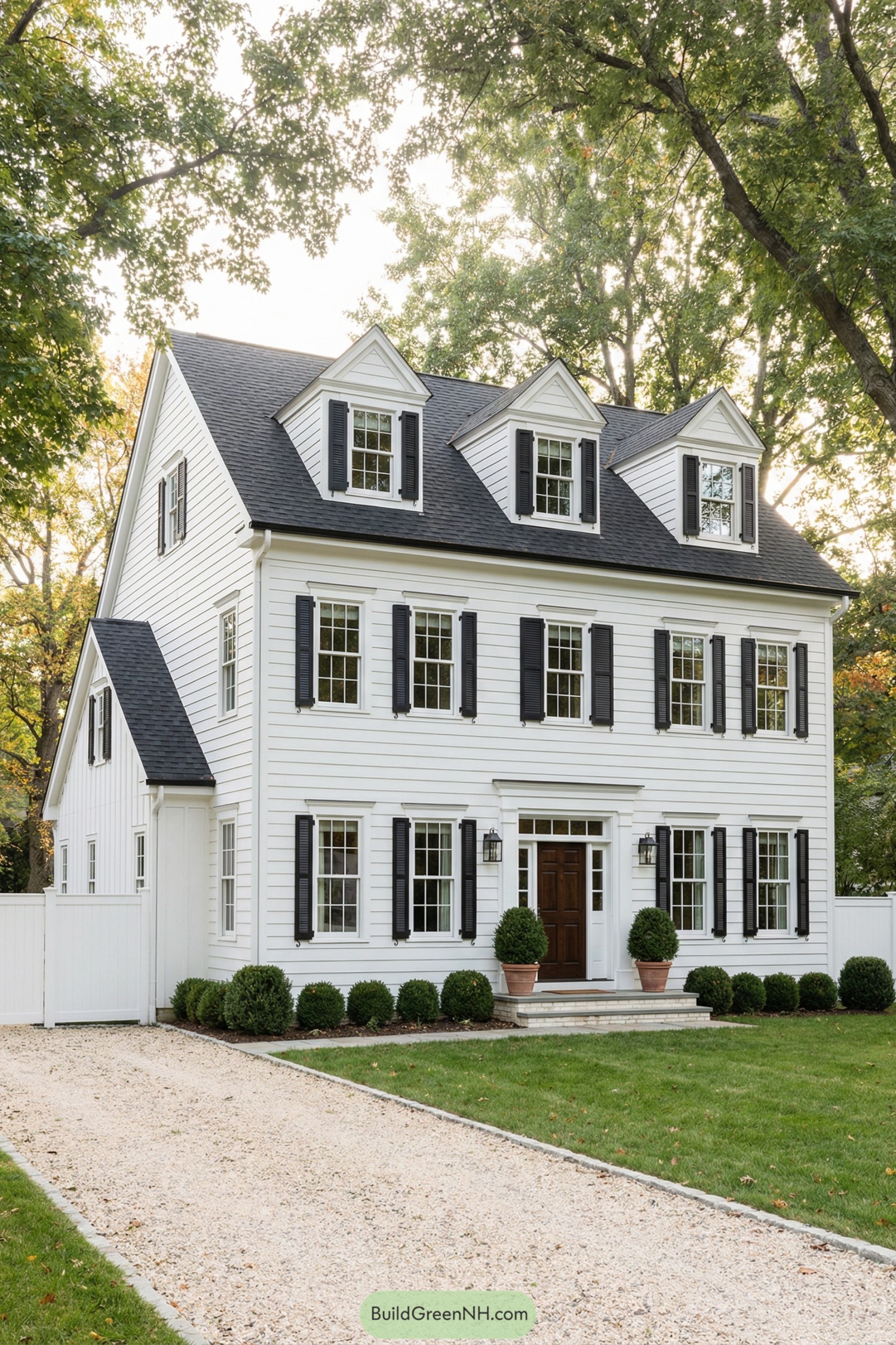 Three story white house with black shutters and dormer windows framed by trees