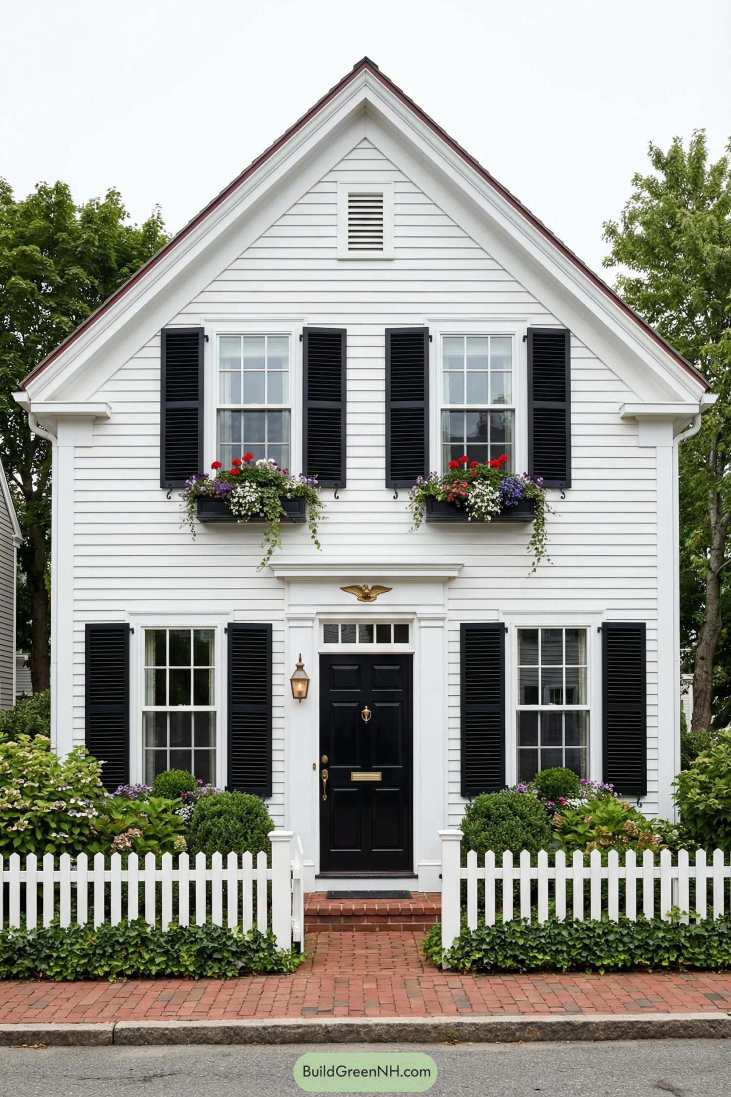 Charming white cottage with black shutters flower boxes and a white picket fence
