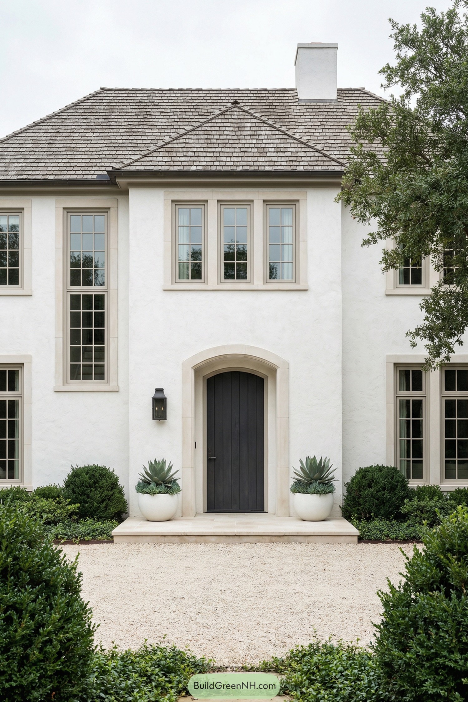 White stucco two story house with arched dark front door and symmetrical tall windows framed by simple landscaping