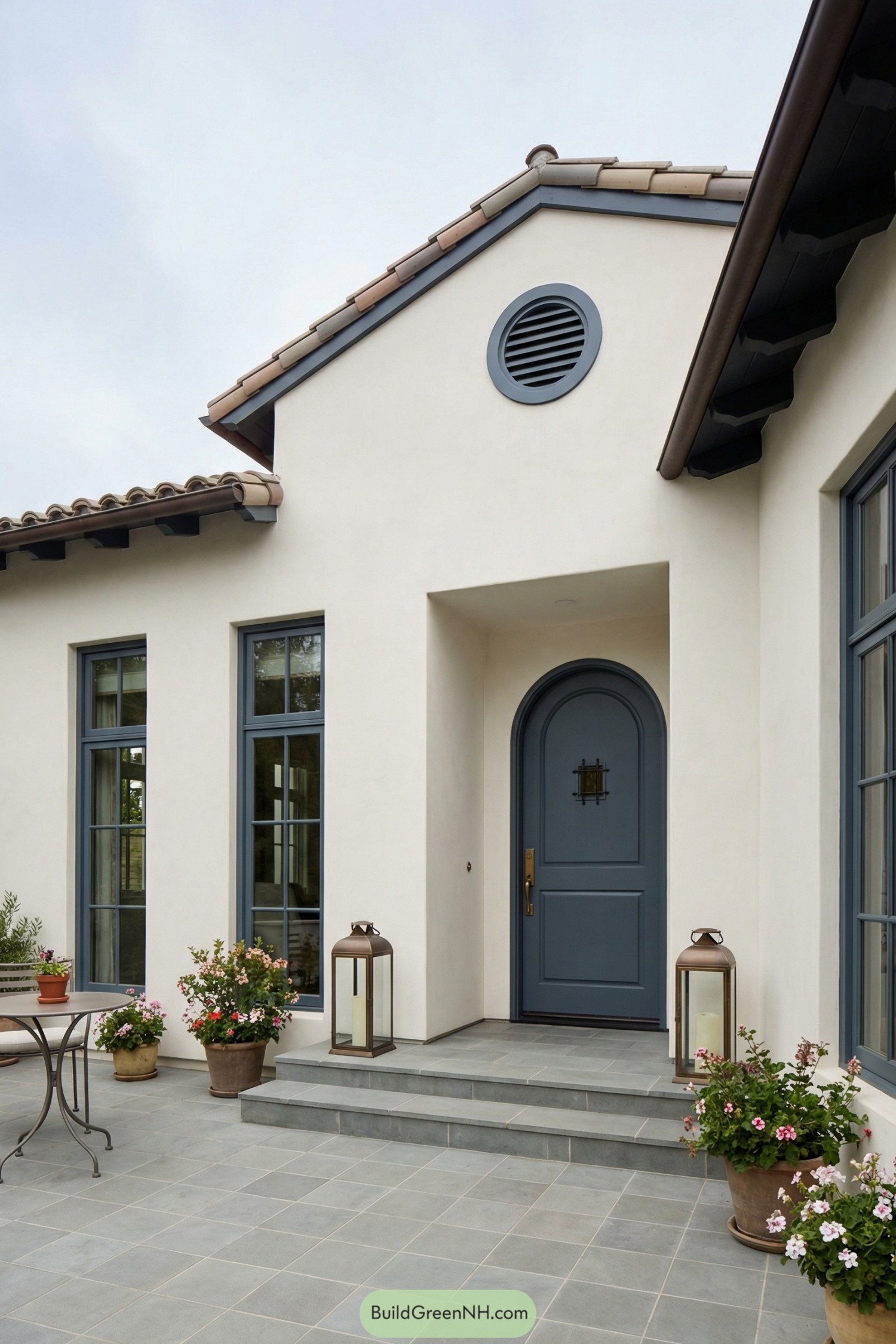 White stucco entry with blue arched door, tall matching windows, tiled porch, and potted flowers