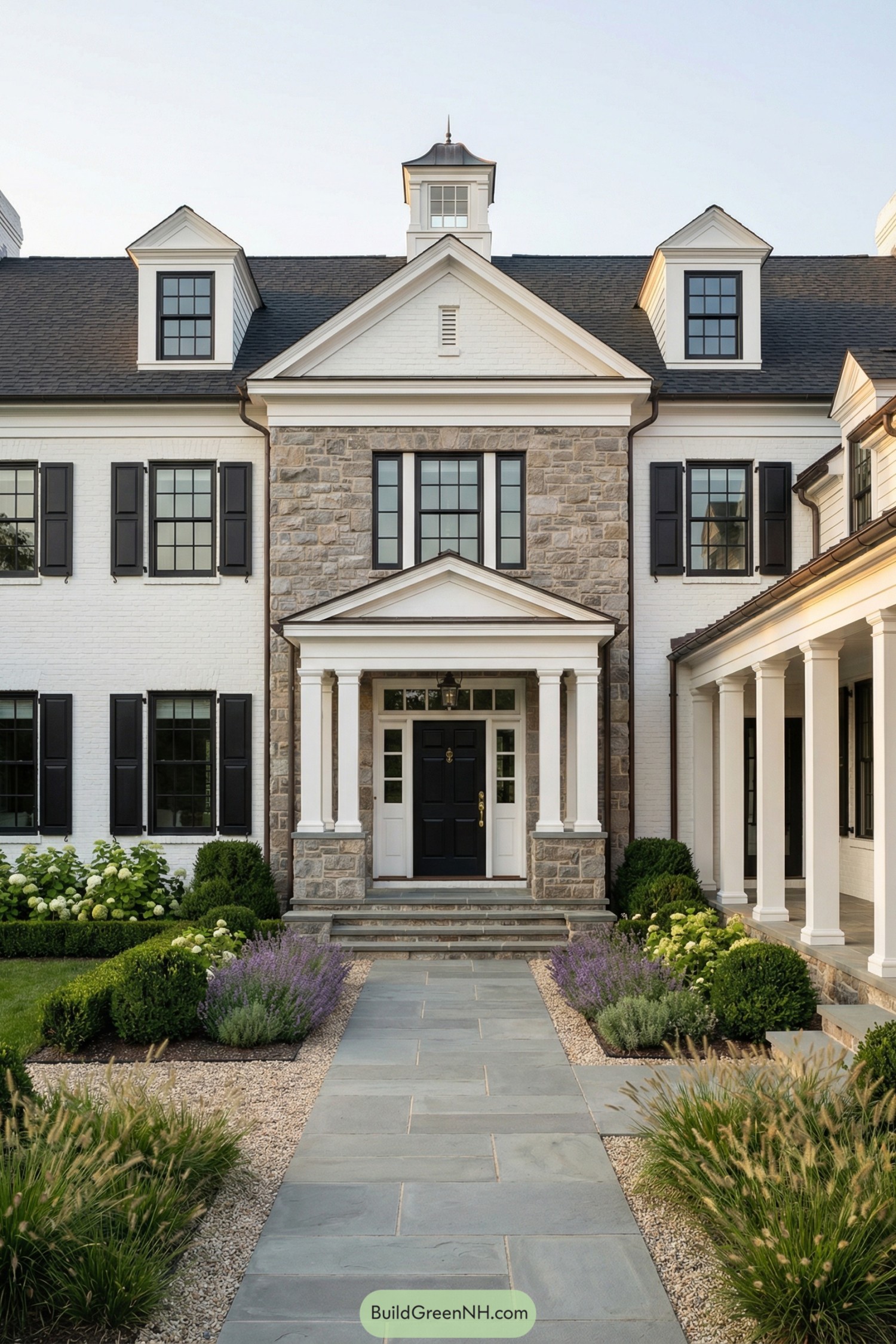 White brick colonial home with stone center bay, black shutters, columned porch, and manicured front garden