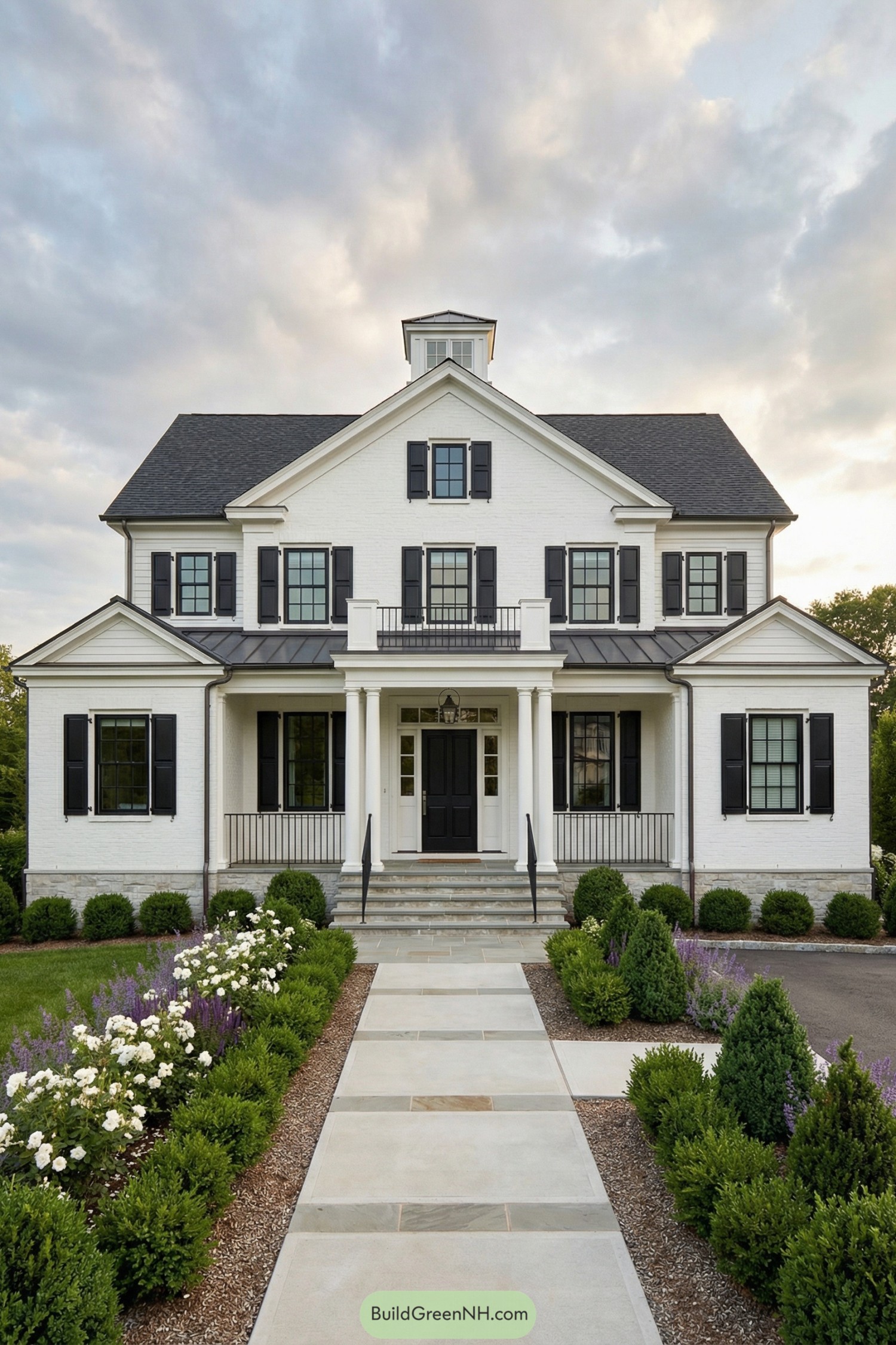 White brick colonial home with black shutters framed by manicured front gardens and a centered walkway