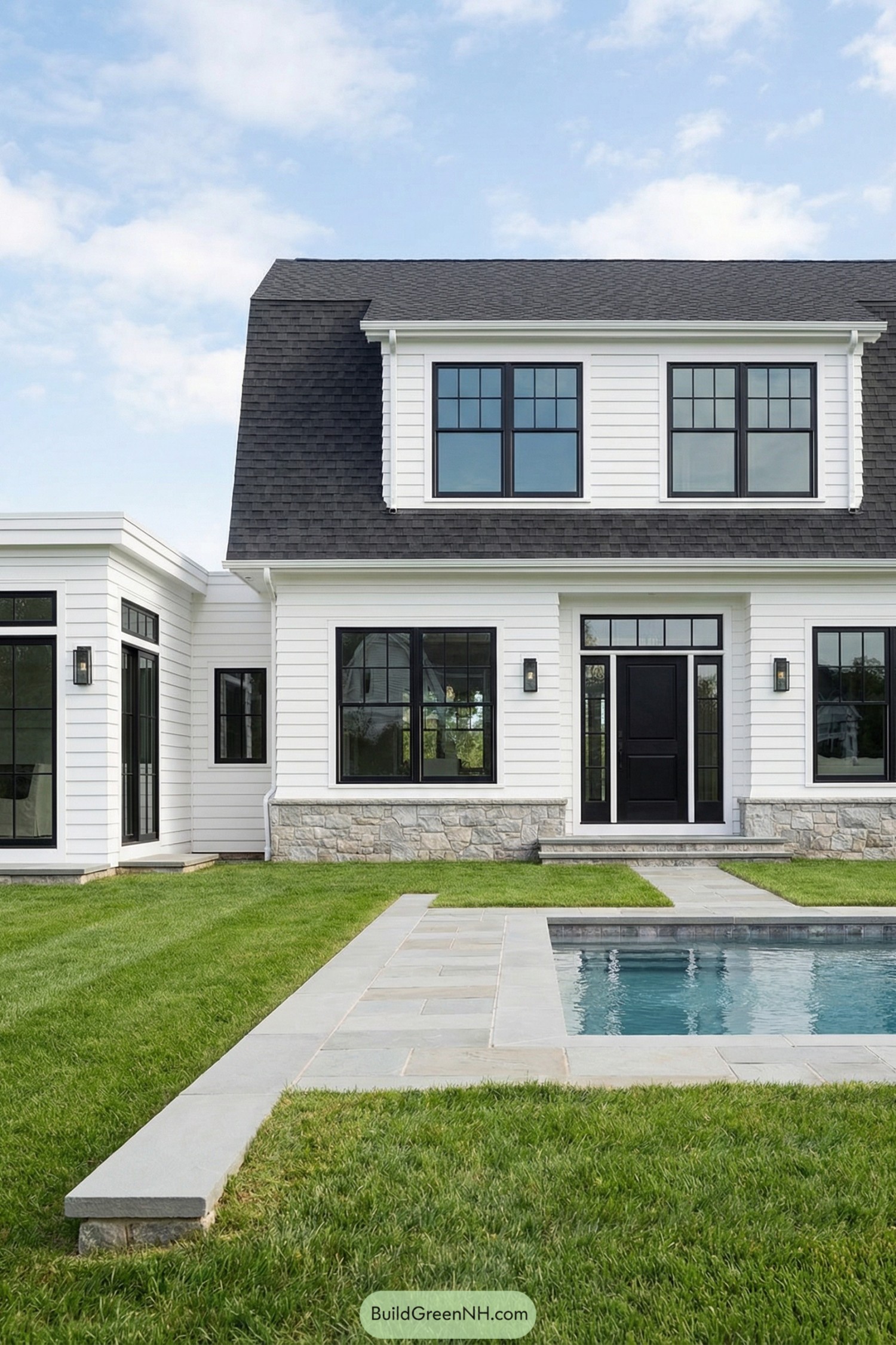 White clapboard Hamptons home with black windows, stone base, and a small rectangular pool in a manicured backyard