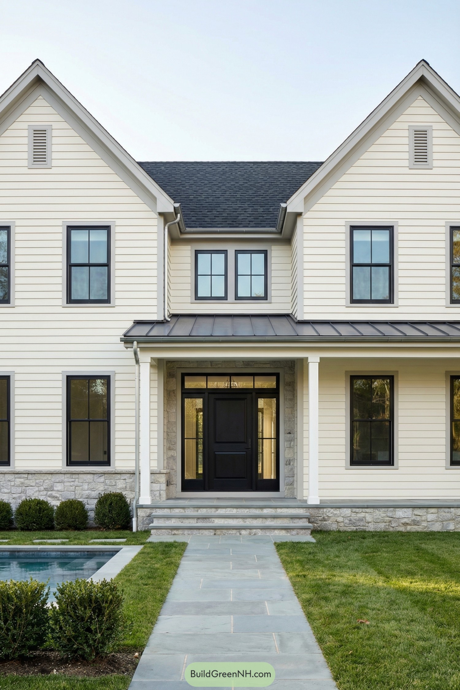 Cream siding farmhouse with black windows and front entry facing a pool and stone walkway