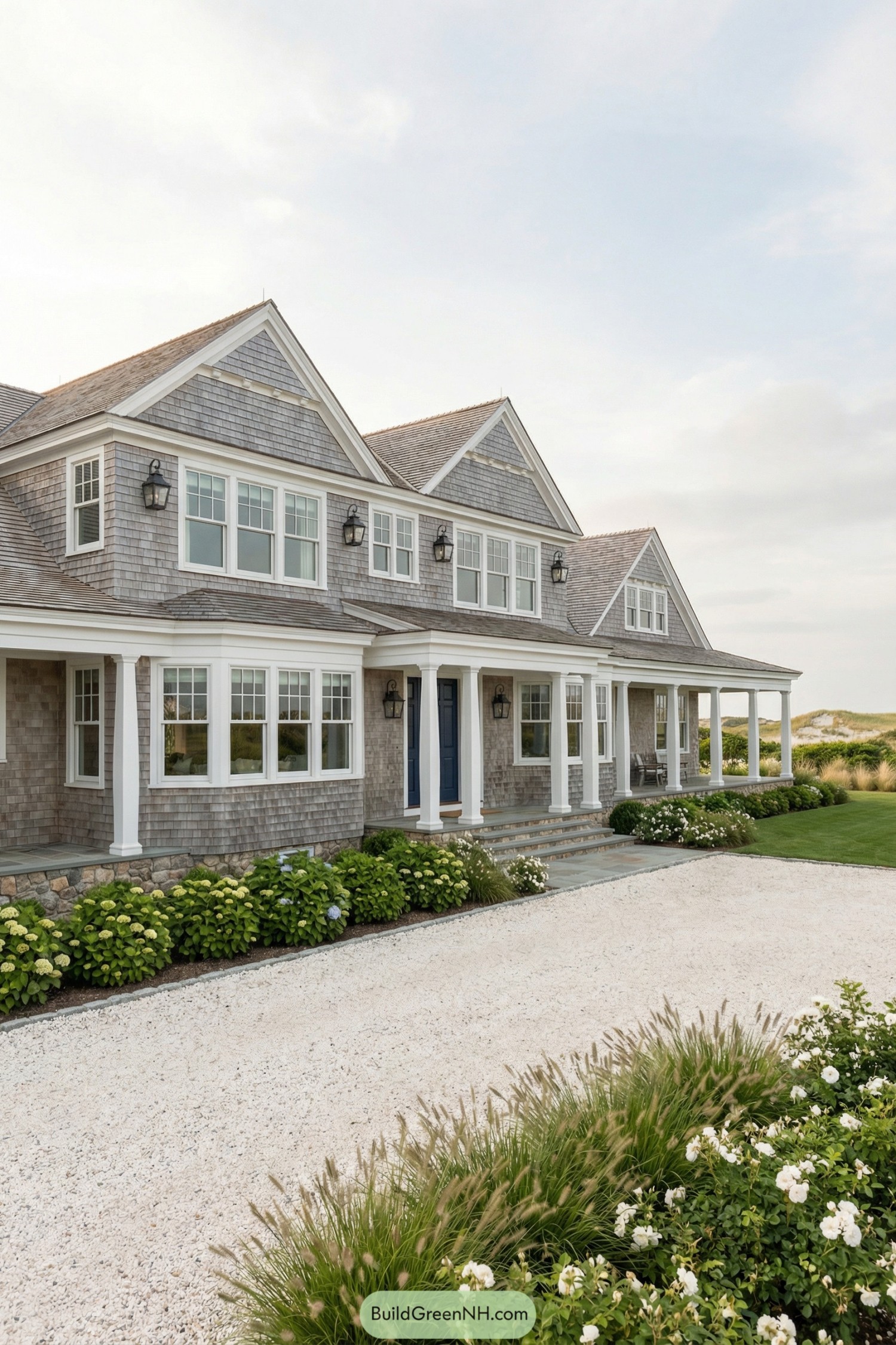Shingle-style coastal mansion with wraparound porch and lush garden beds