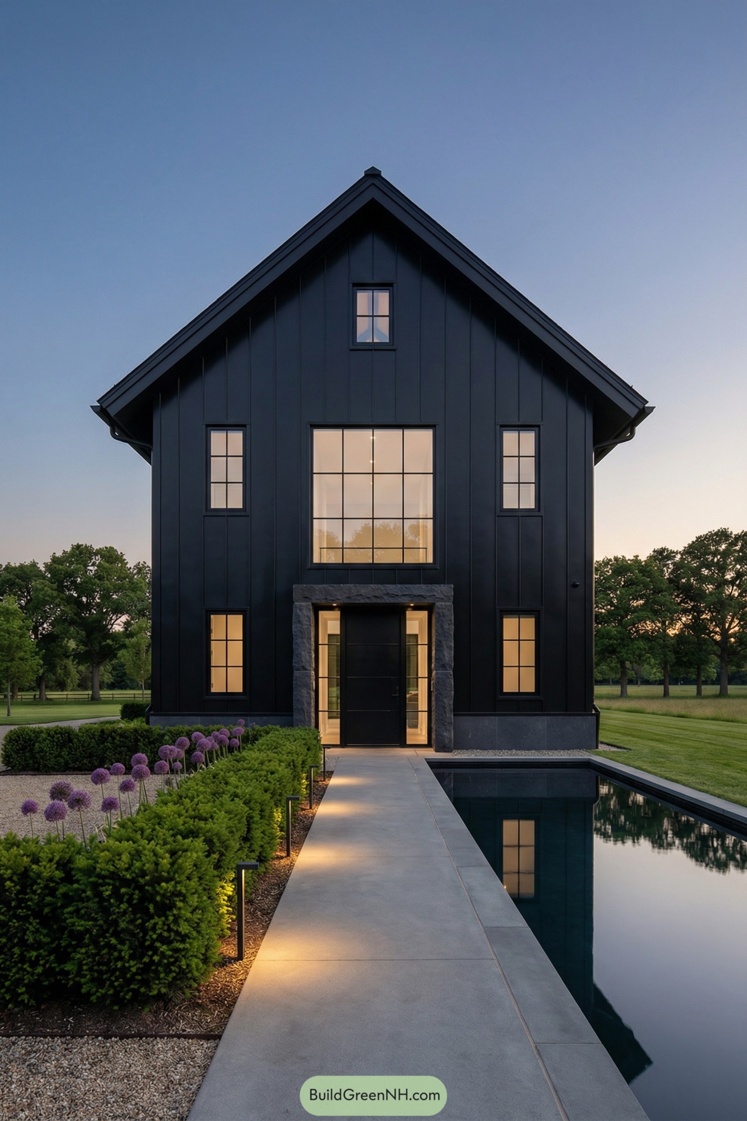 Tall black barndominium with reflecting pool and trimmed landscaping at dusk