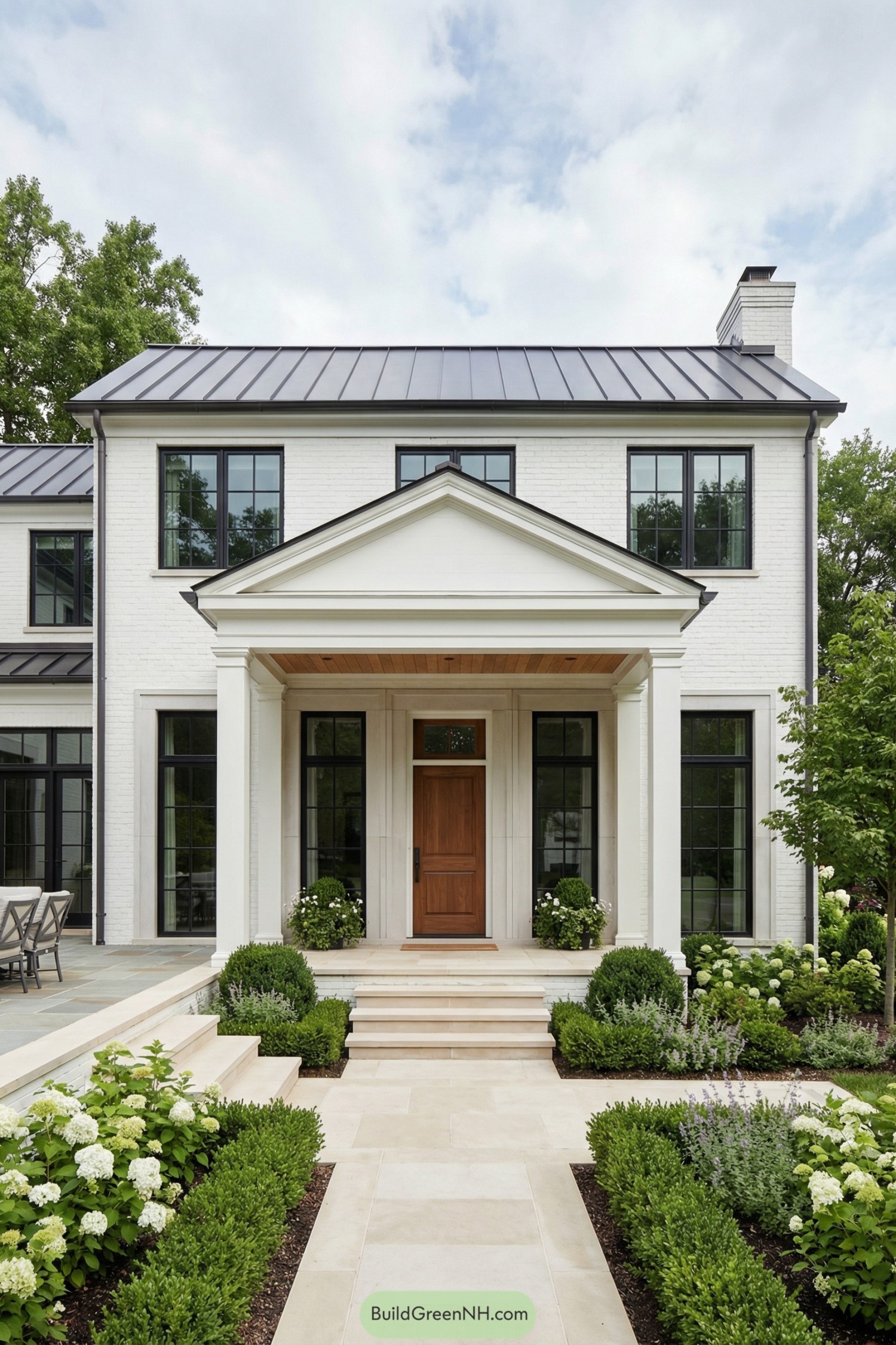White brick two story house with metal roof, columned entry porch, black framed windows and formal front garden