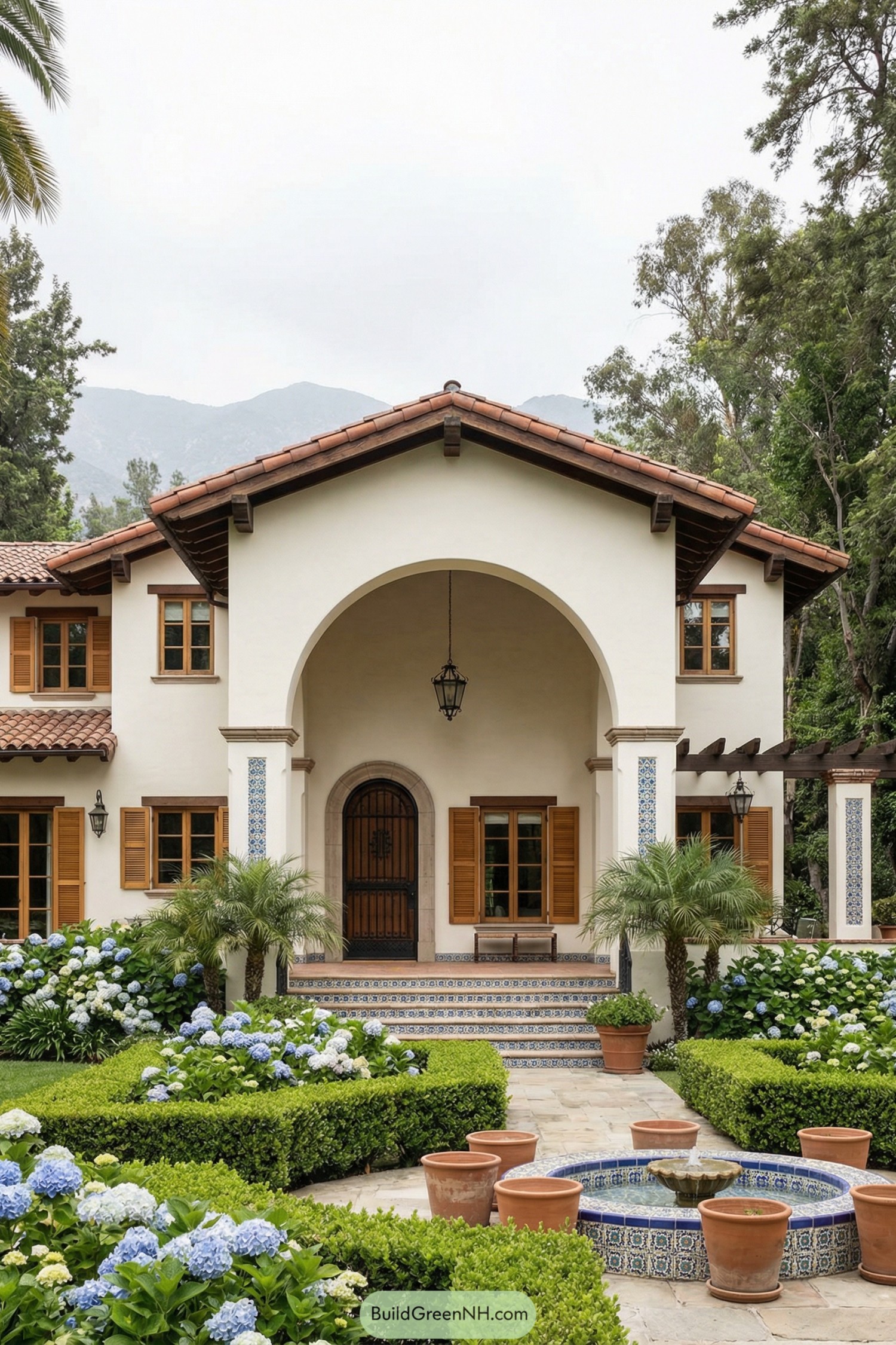 Spanish-style villa with arched entry, tiled fountain, and lush hydrangea garden