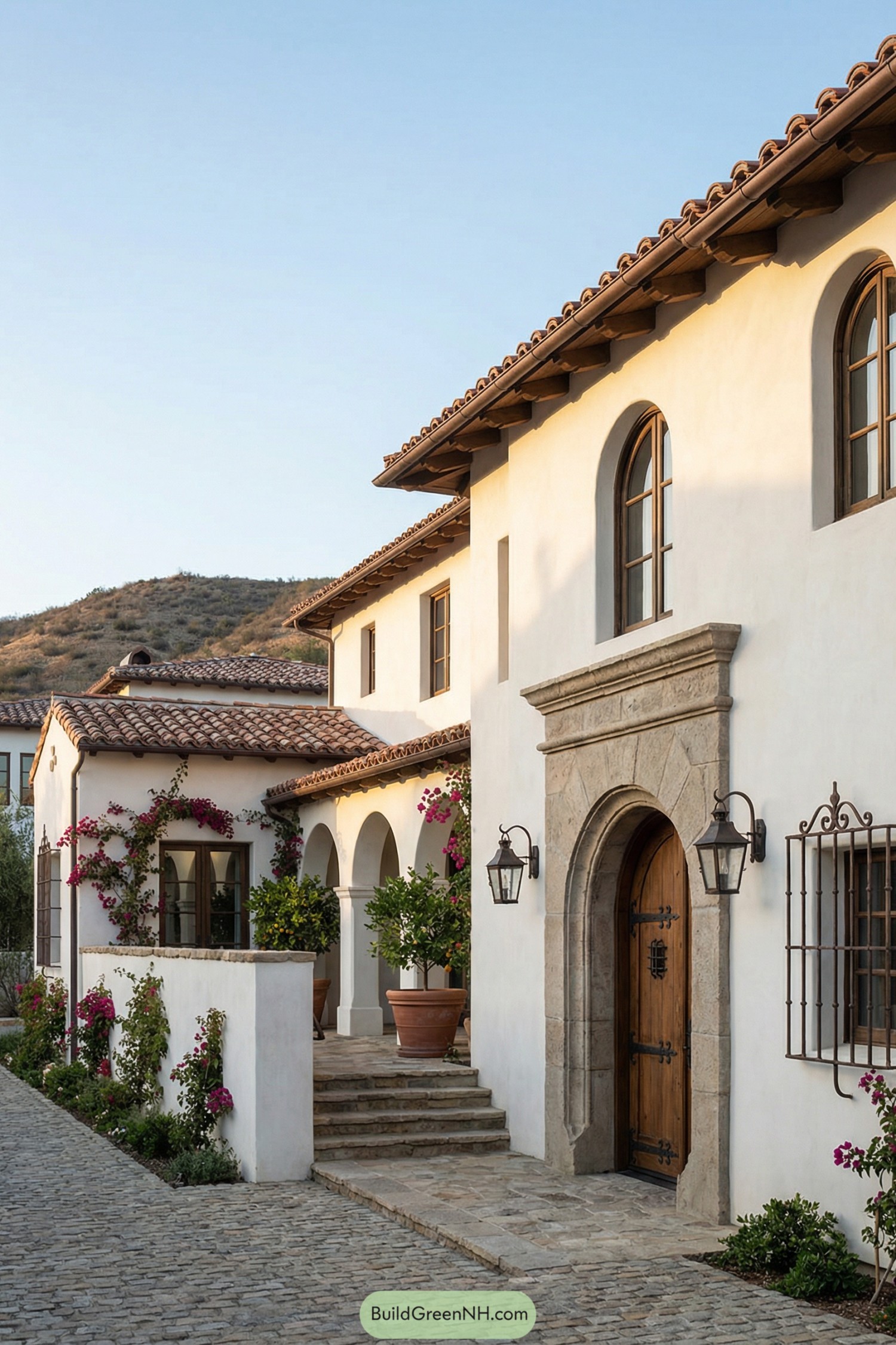 Stucco Spanish-style house with tiled roofs and arched entry facing a cobblestone drive