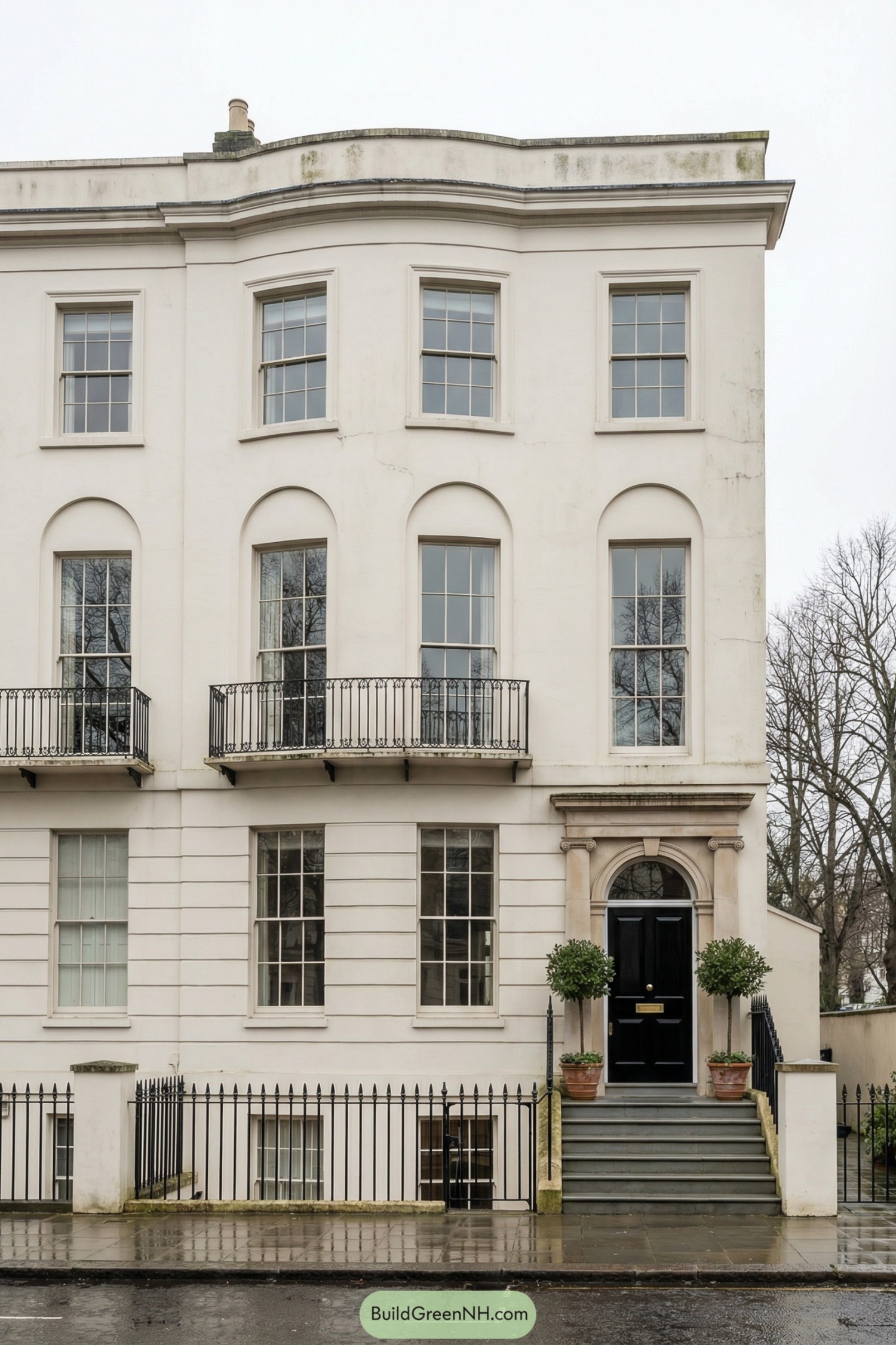 Elegant white stucco corner townhouse with arched windows, iron balconies, and a grand black front door