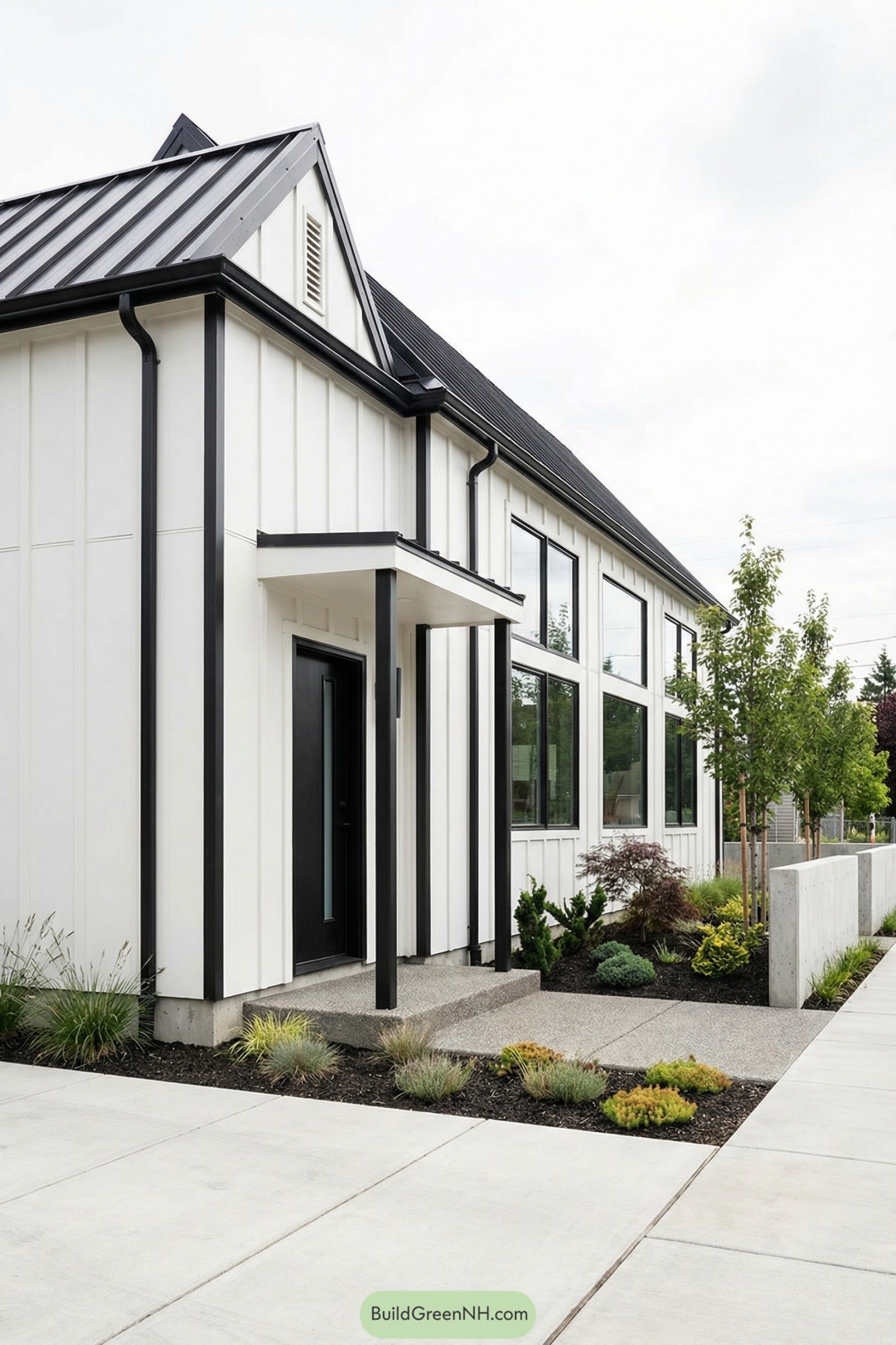 Modern white barndominium with black metal roof, tall windows, and minimalist front entry landscaping