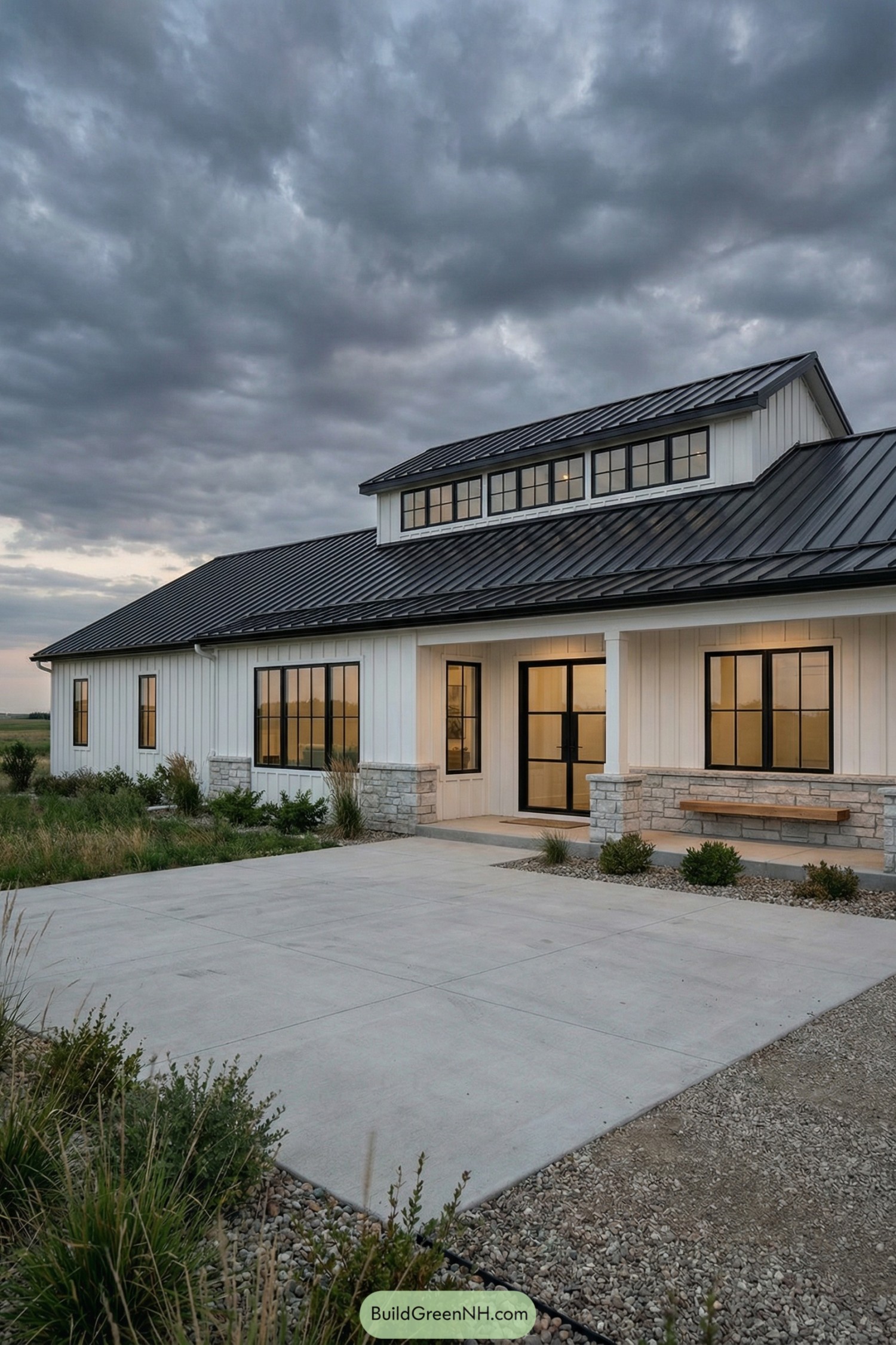 Modern white barndominium with black metal roof, large windows, and stone accents at sunset