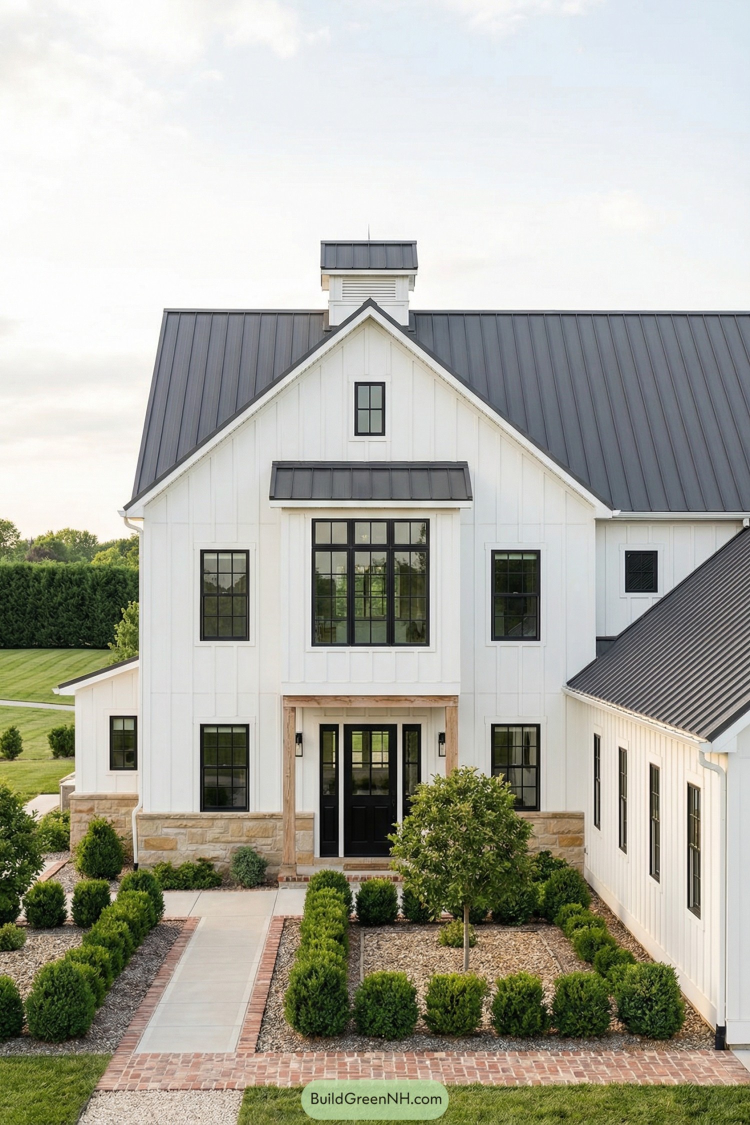 White modern farmhouse with black metal roof and manicured front courtyard