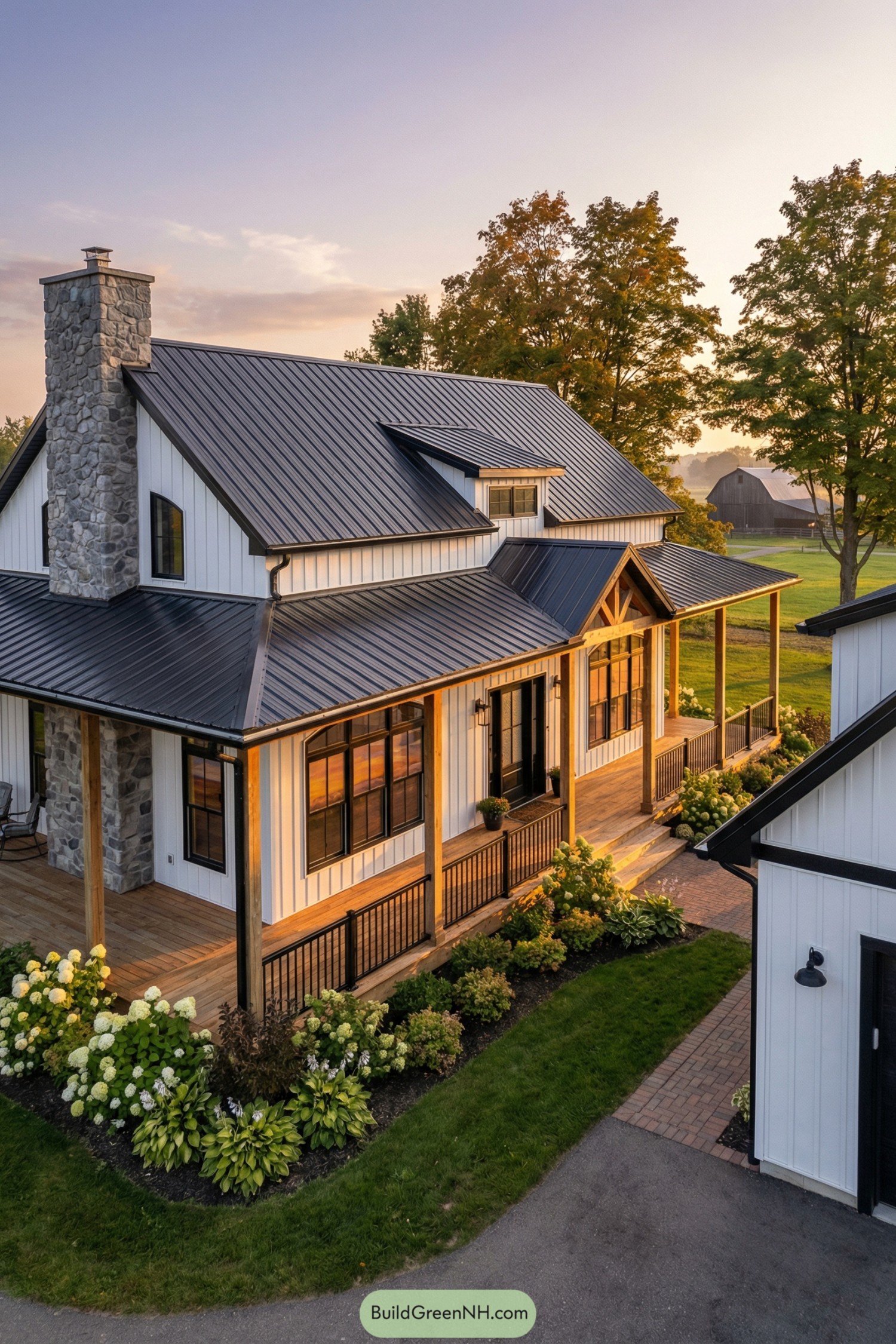 High-res photo of modern farmhouse barndominium with a white gabled facade and a prominent stone chimney anchoring one corner, paired with a wraparound veranda and modern black trim; bright white siding with gray stone and black-framed details; long main barndo rectangle with a perpendicular garage/shop volume creating a courtyard-like front approach; board-and-batten siding with natural fieldstone chimney and porch bases; dark graphite standing-seam metal roof with two aligned gables and a small dormer; evenly spaced grid windows in black frames with slightly arched top transoms at the main gable; a single black metal entry door with frosted glass panel and matching sidelights; broad wooden porch deck with rocking-chair spacing, timber truss accent at the gable, and a brick-edged walkway; lush landscaping with hydrangeas, hostas, and layered shrubs against the porch line; mature maples and a distant barn silhouette beyond a clipped lawn; golden-hour light with warm window reflections and long shadows across the veranda floor, single real-life photo, high-resolution, architectural photography, soft lighting, cinematic composition, strictly no collages.