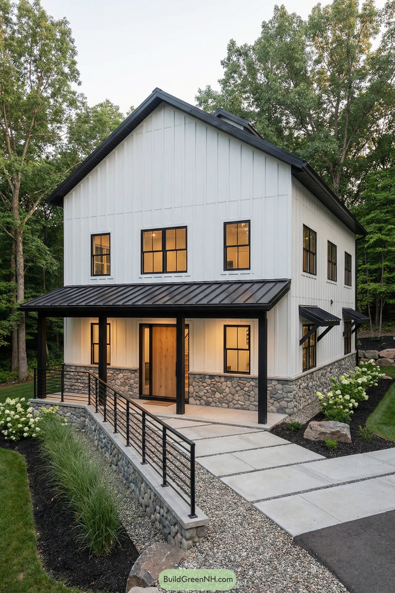Two story white barndominium with stone base and black metal porch set among trees