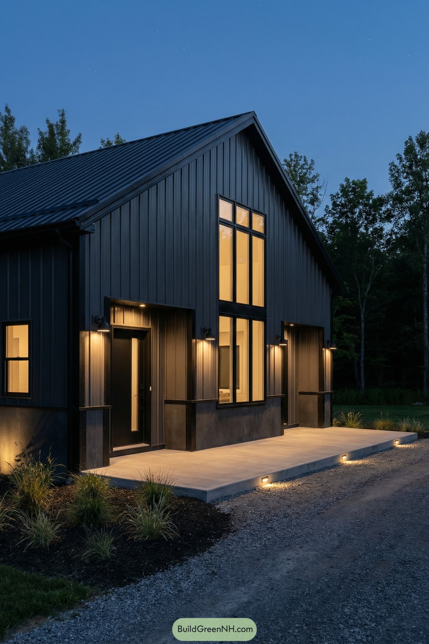 Dark charcoal barndominium with tall windows glowing warmly at dusk