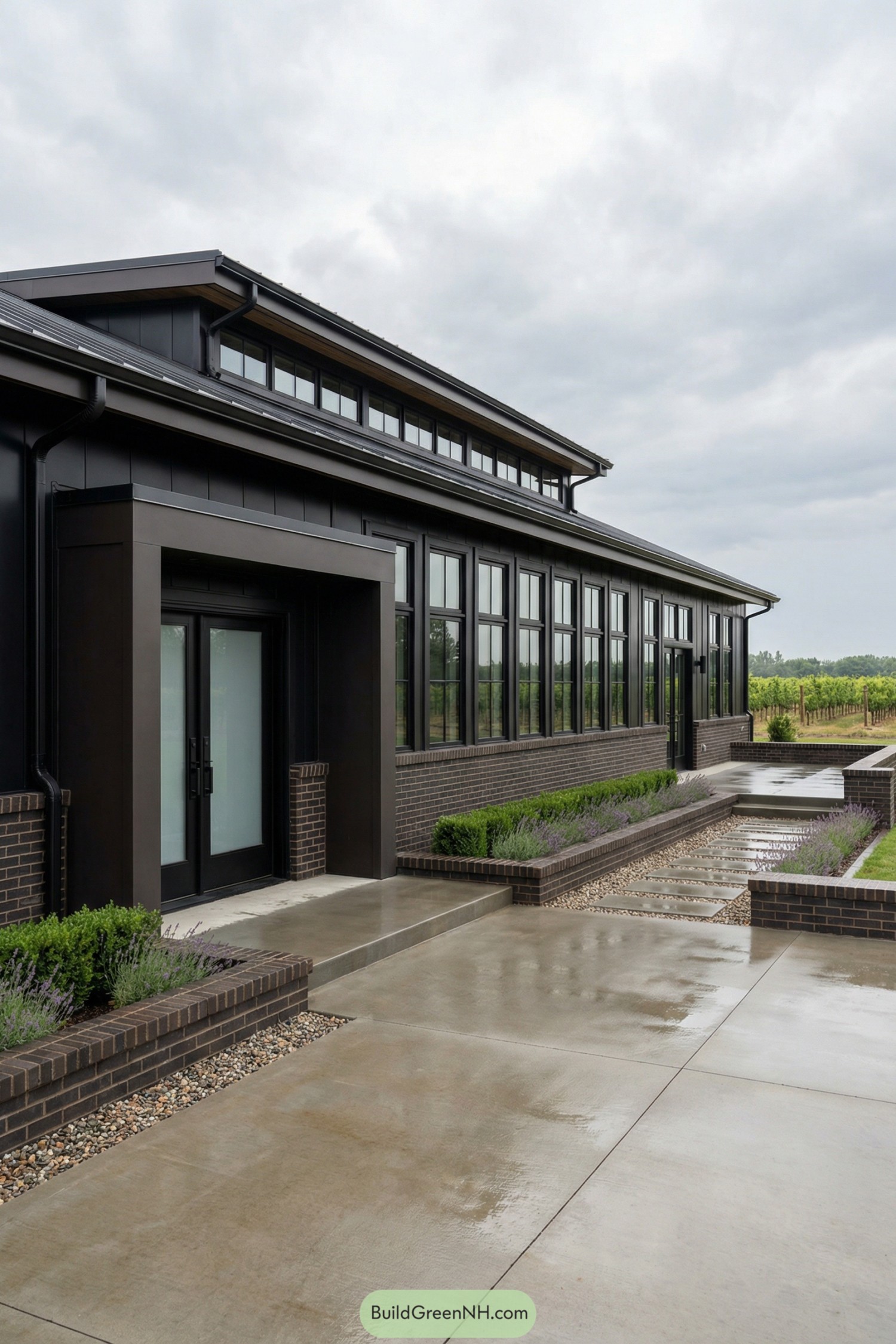 Dark metal barndominium with brick base and long windows by a landscaped walkway