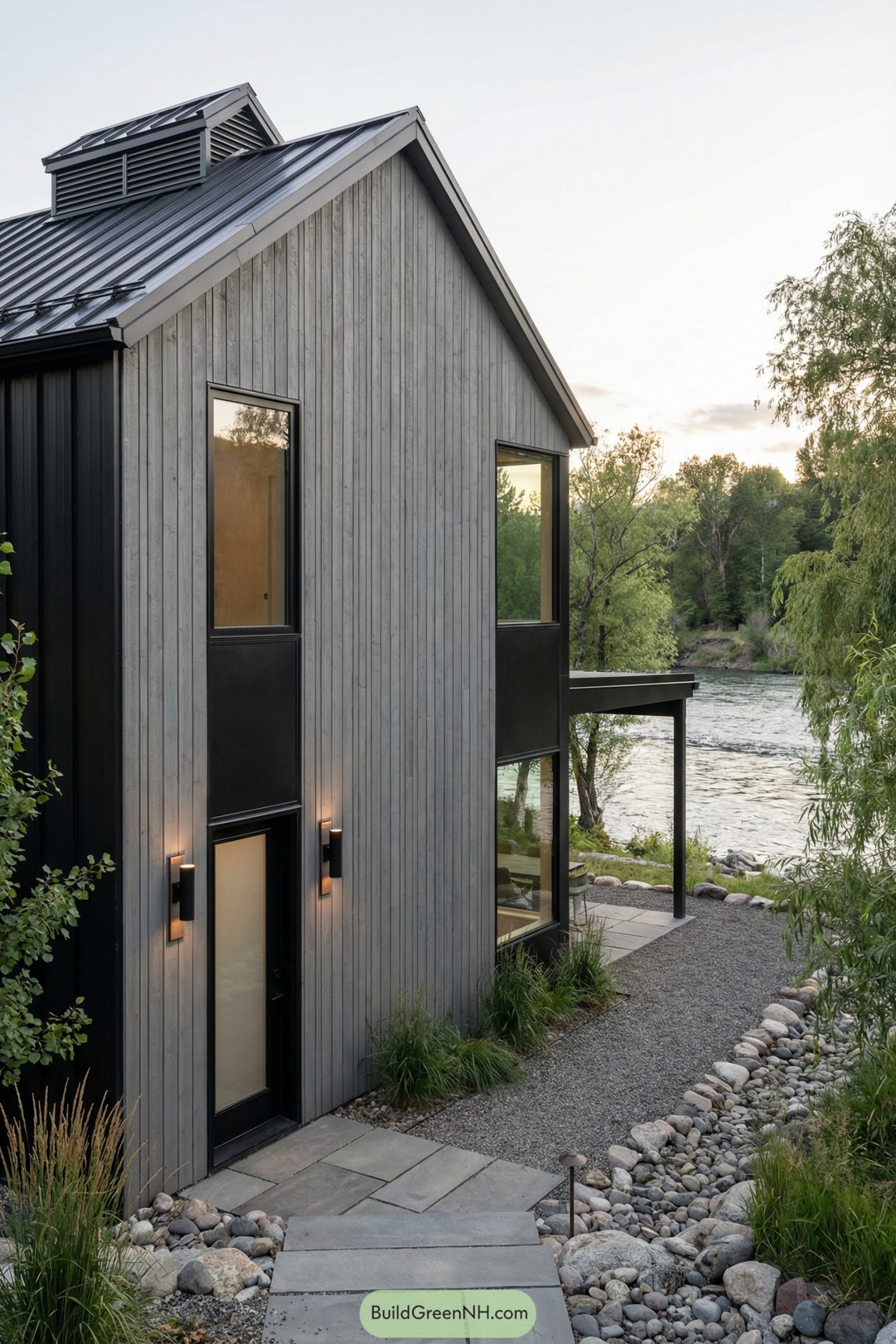 Two story grey barndominium with tall windows and metal roof set along a riverbank