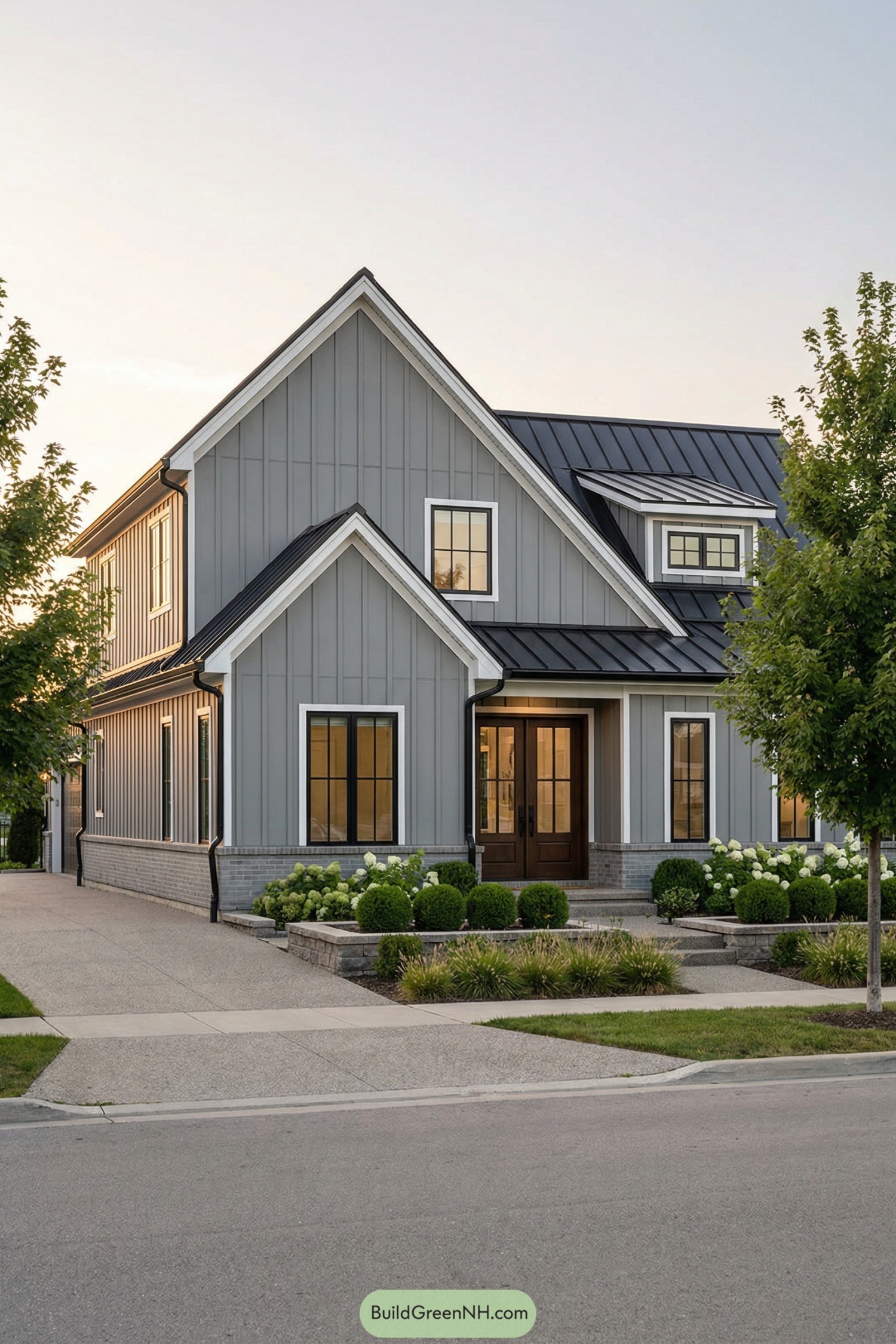 Grey barndominium style home with steep gables black metal roof and manicured front landscaping