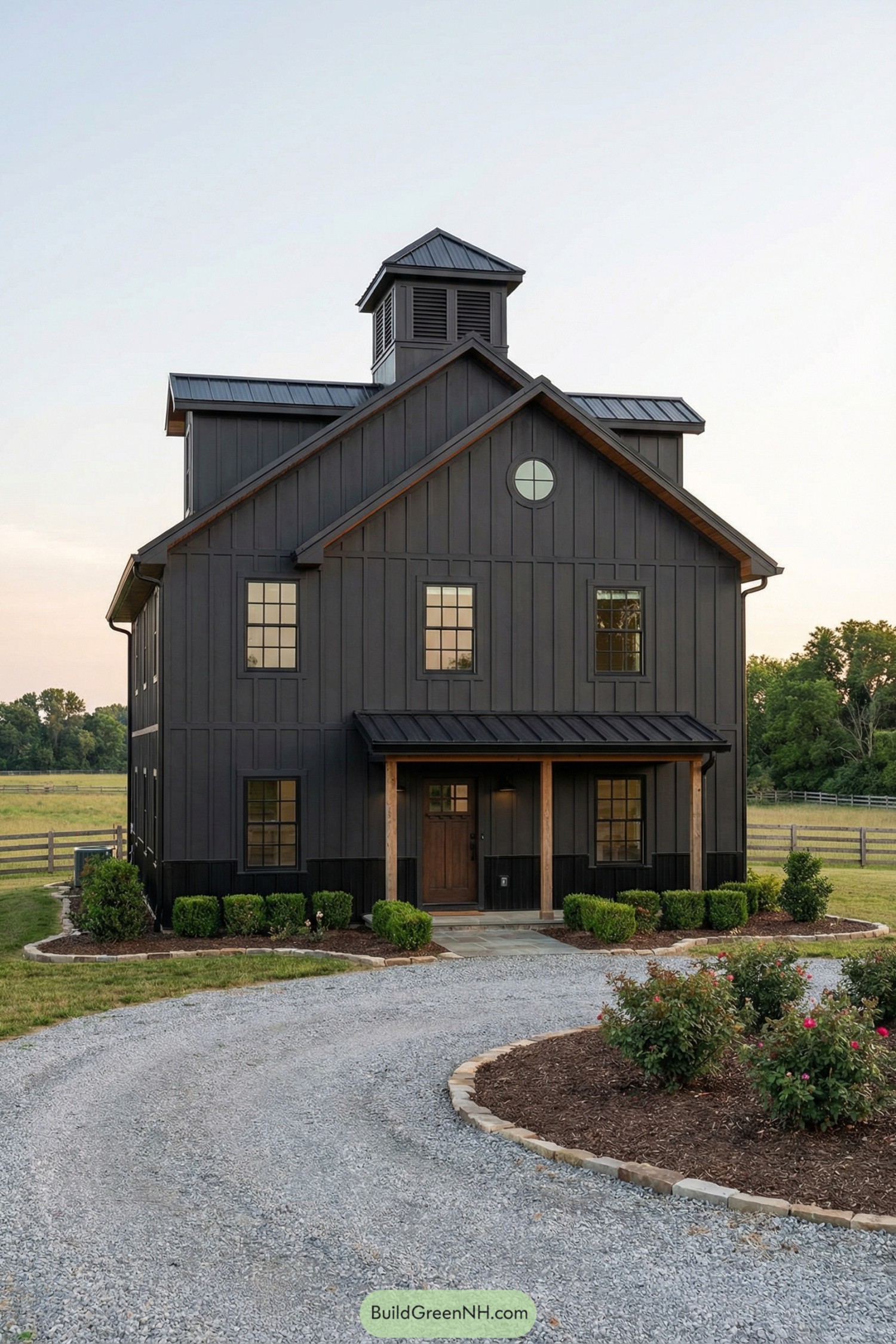 Dark modern barn-style home with cupola and gravel drive on a rural lot