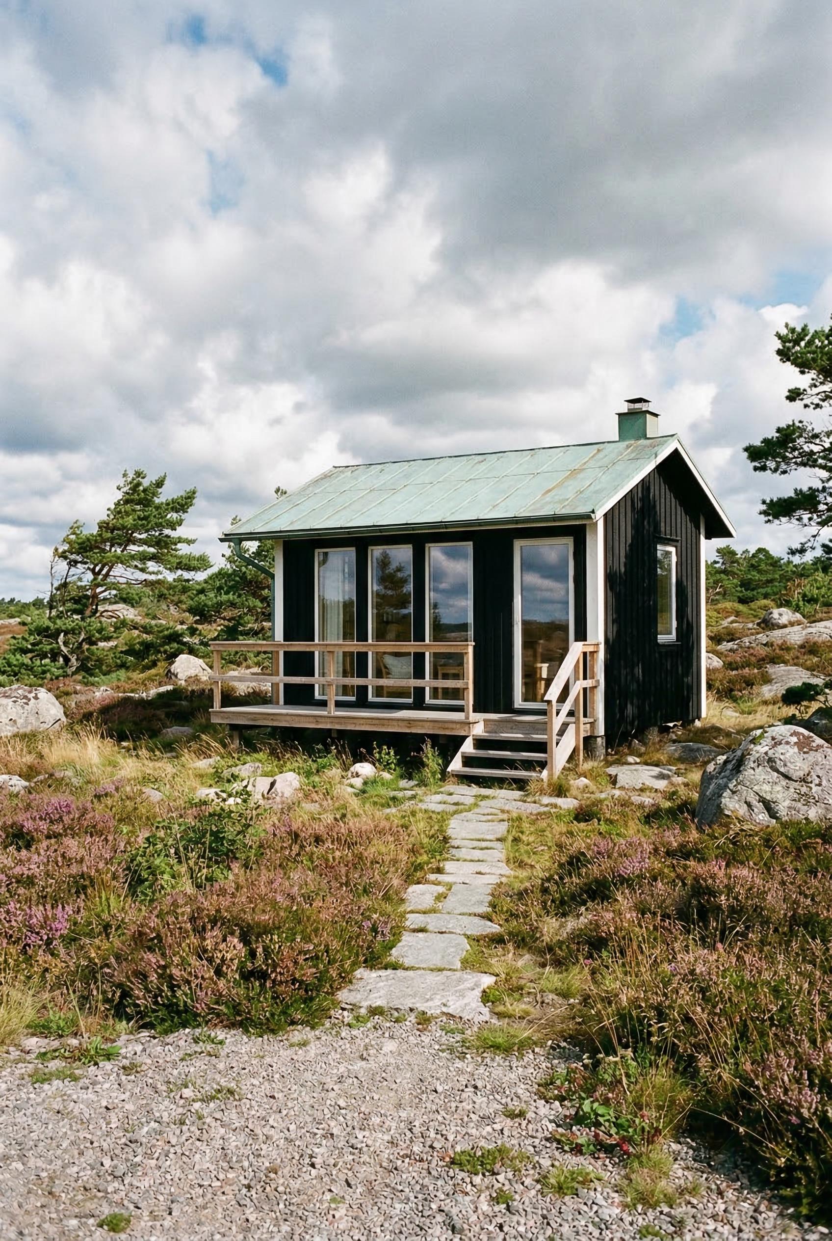 Small black cottage with green metal roof in rocky heath