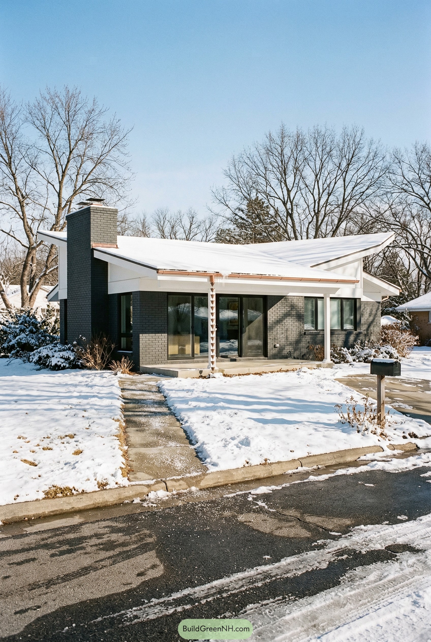 Dark gray brick ranch with folded white roof in snow