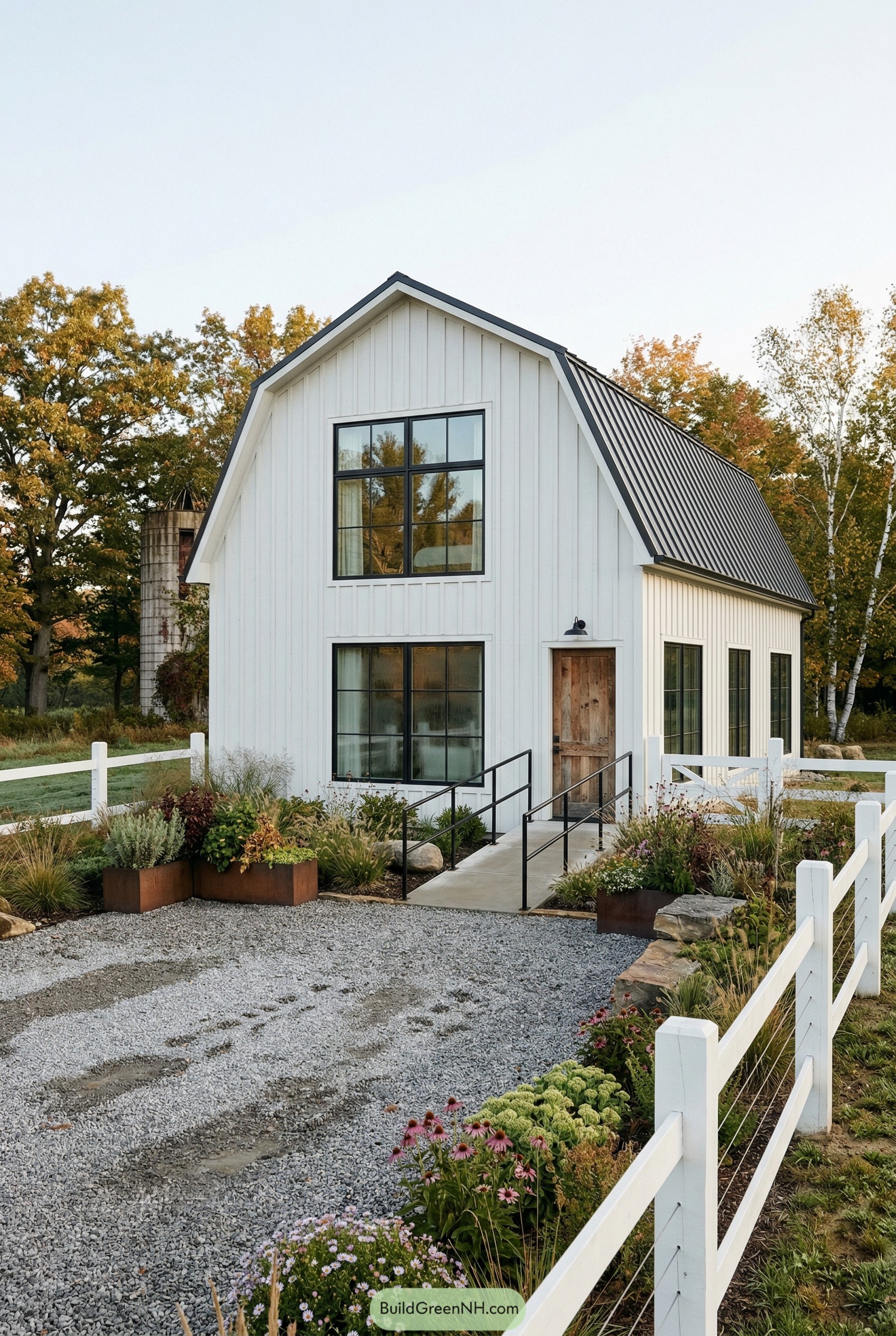 White barn style house with black metal roof and white fence
