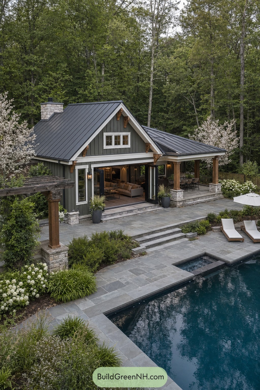 Modern craftsman pool house with dark metal roof and stone patio beside a backyard pool