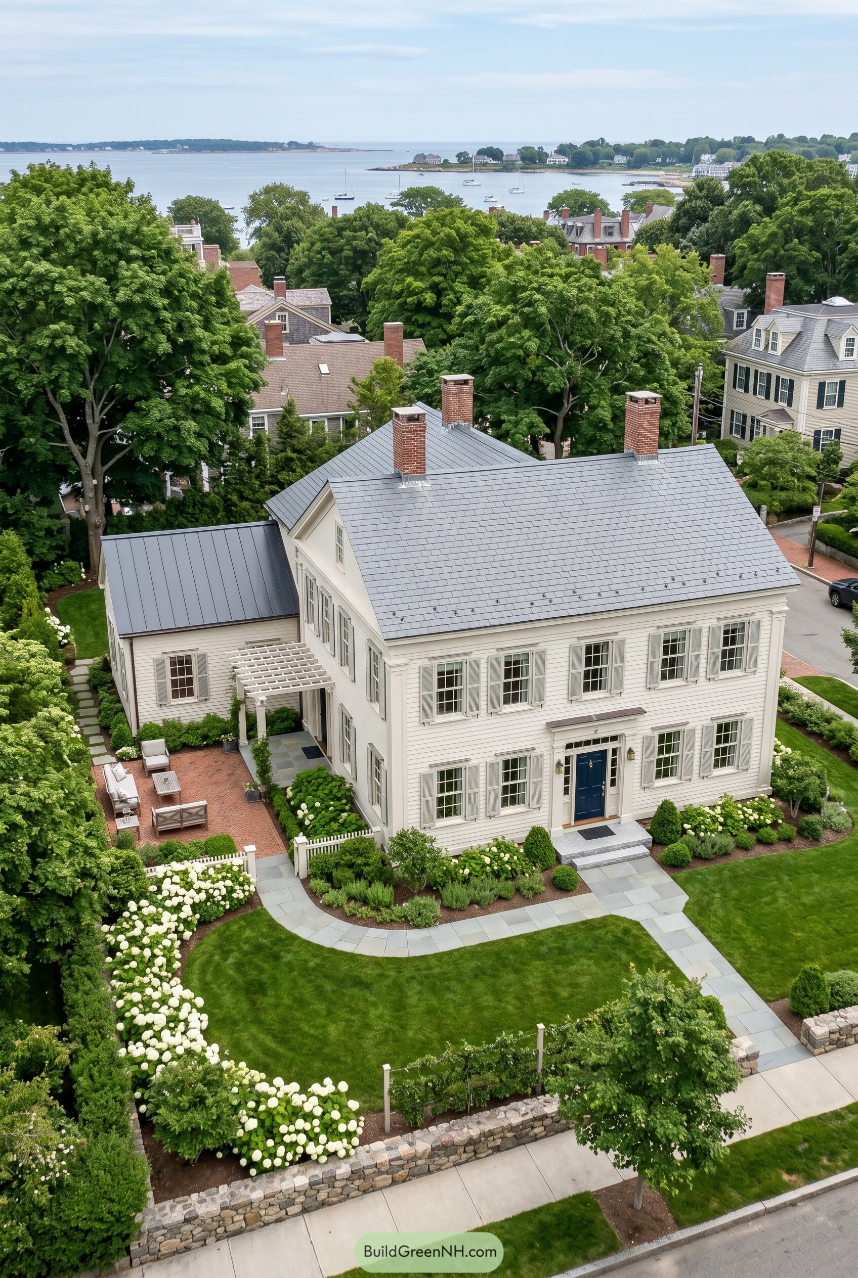 Aerial view of a white coastal house with slate roof and formal garden near the water
