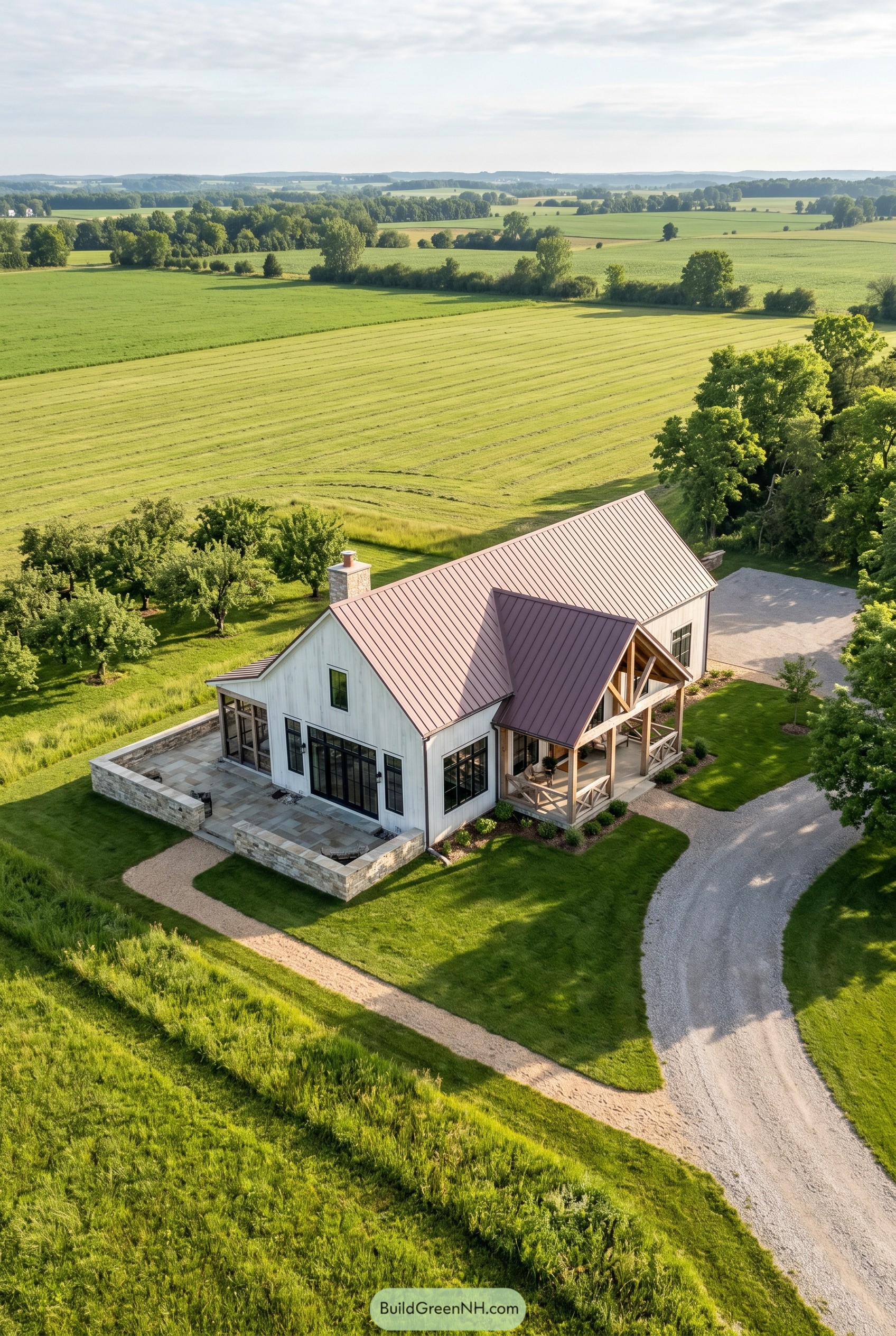 White barndominium with rose metal roof and stone patio in open farmland