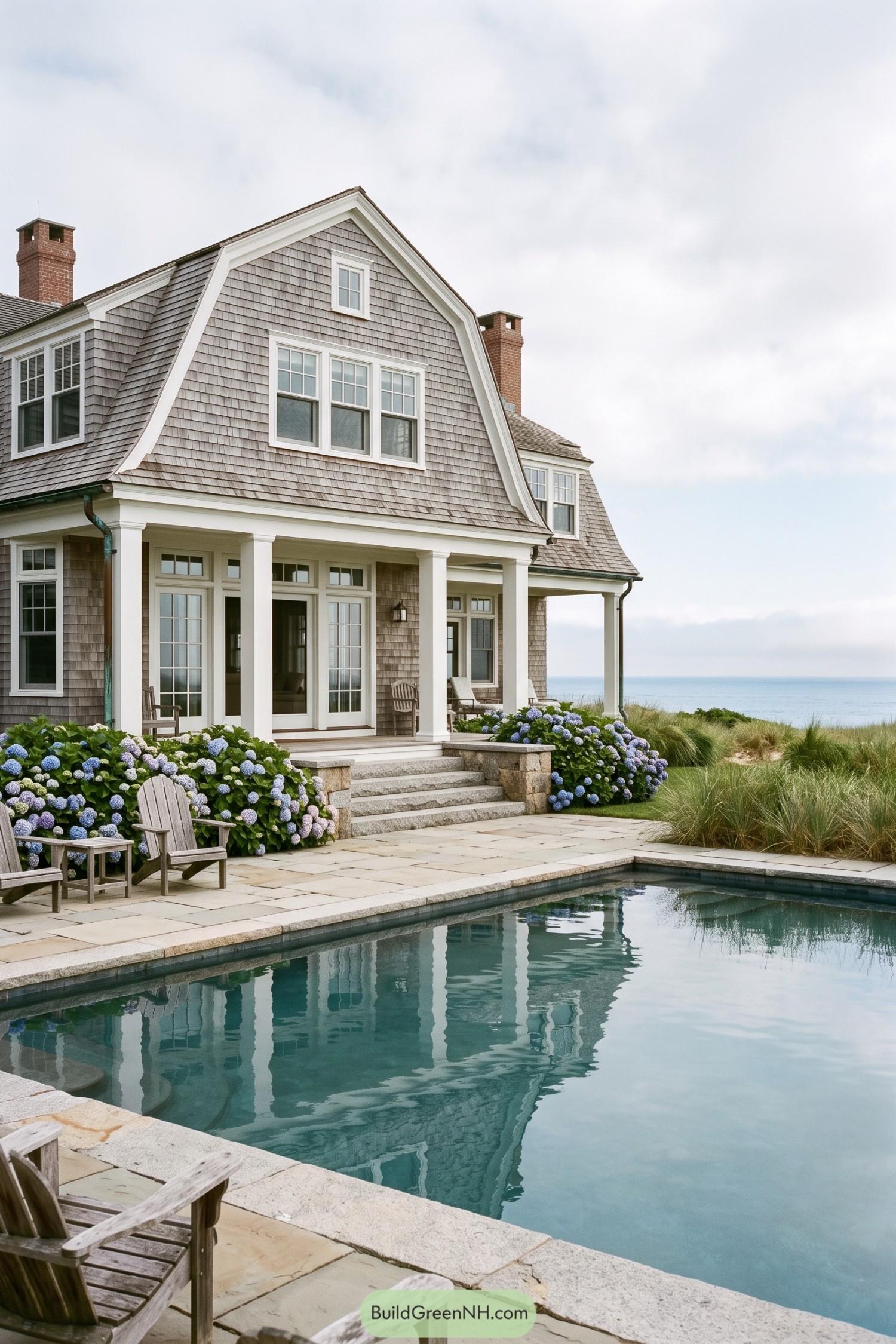 Stone pool terrace with hydrangeas beside a shingled coastal home overlooking the ocean