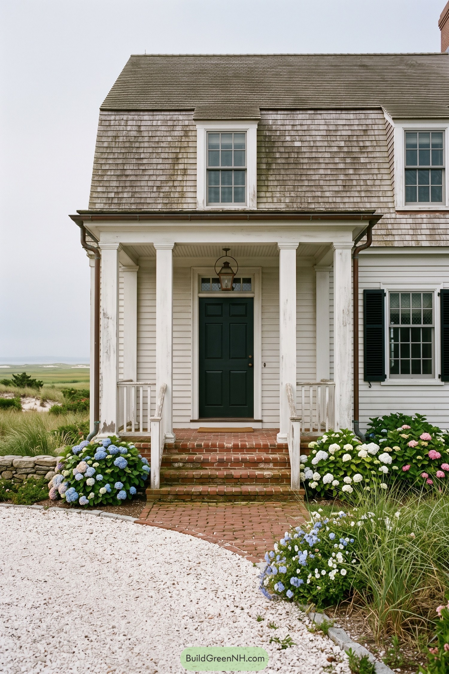 Weathered shingle home with white porch and dark green door