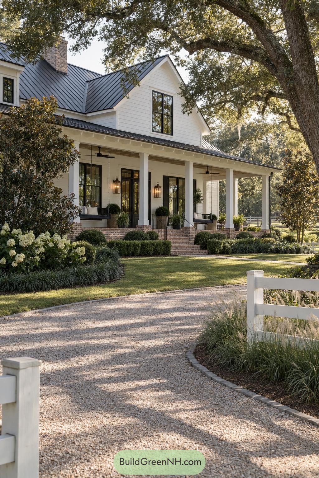 White farmhouse with black metal roof and wraparound porch beneath mature oaks