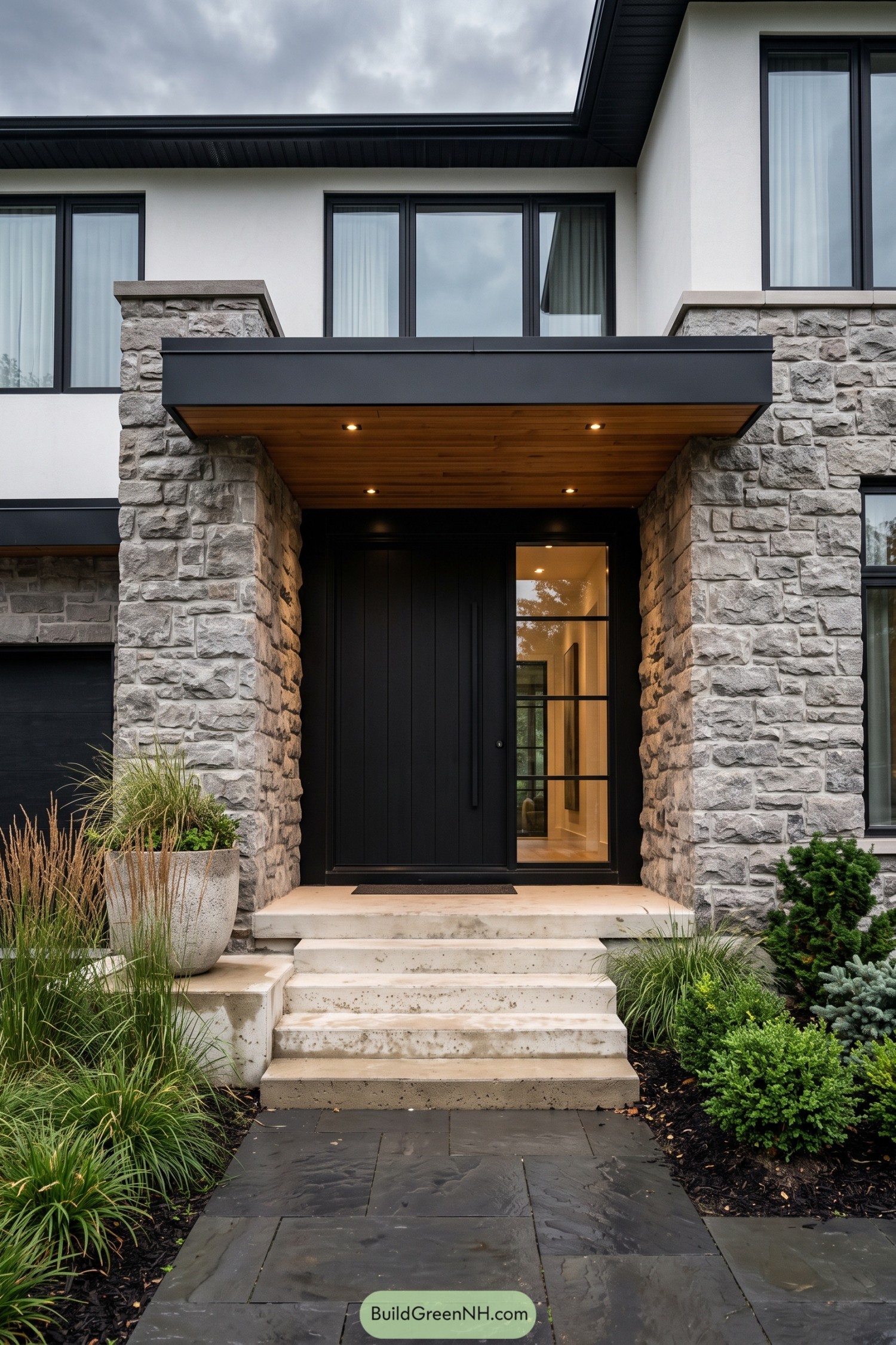Black paneled front door with glazed sidelight between stone pillars