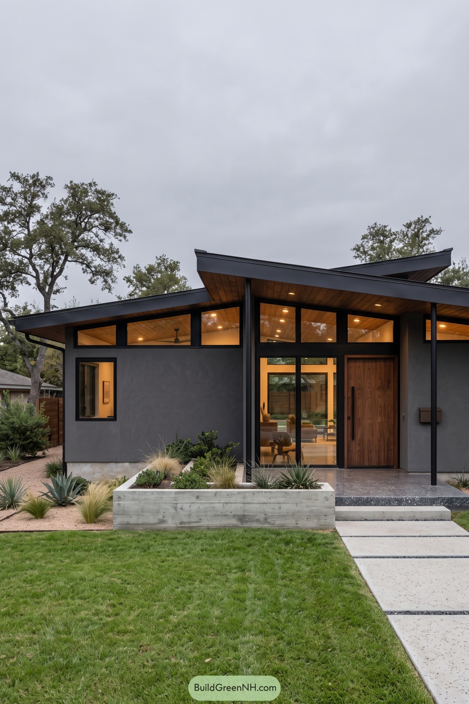 Charcoal house with overlapping sloped roofs, wood soffits, tall windows, and a concrete planter beside the entrance