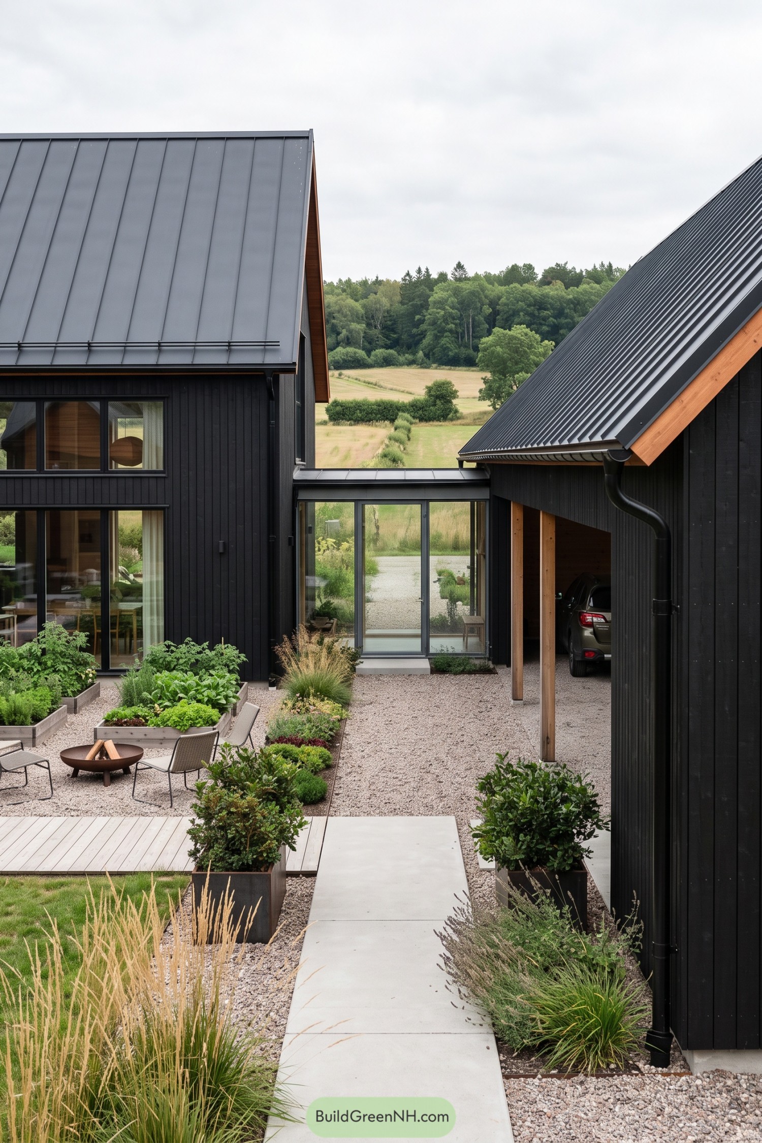 Black timber barn house with metal roofs overlooking a gravel courtyard with raised beds and a fire bowl