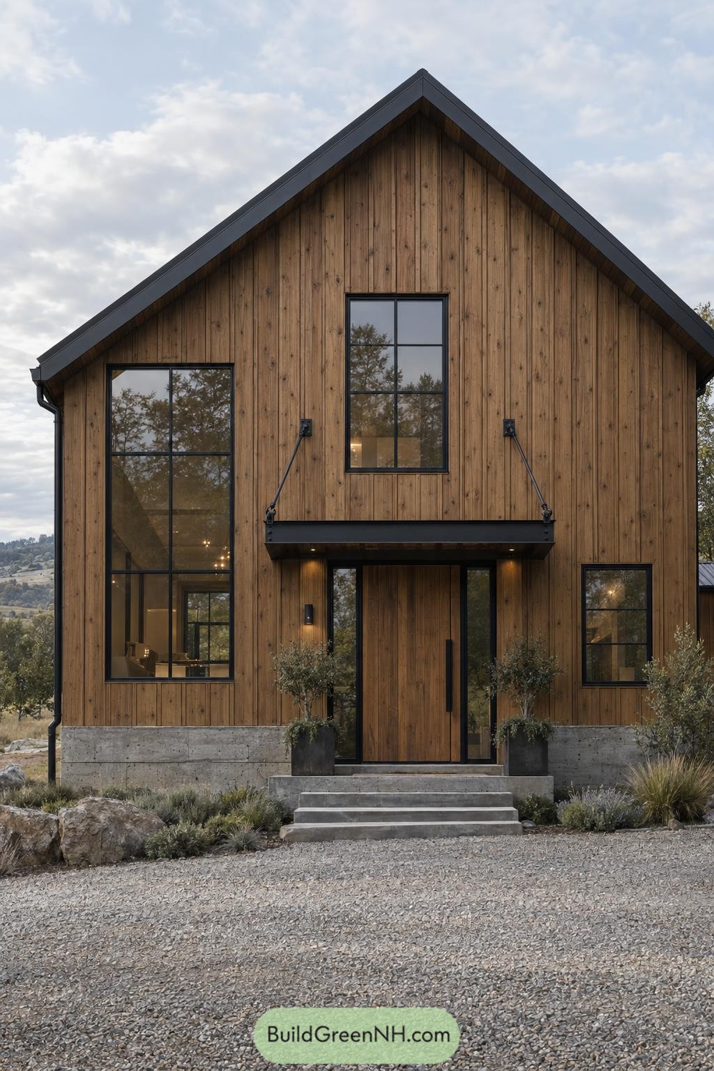 Wooden front facade with a steep gable roof, black framed windows, a suspended entrance canopy and concrete steps